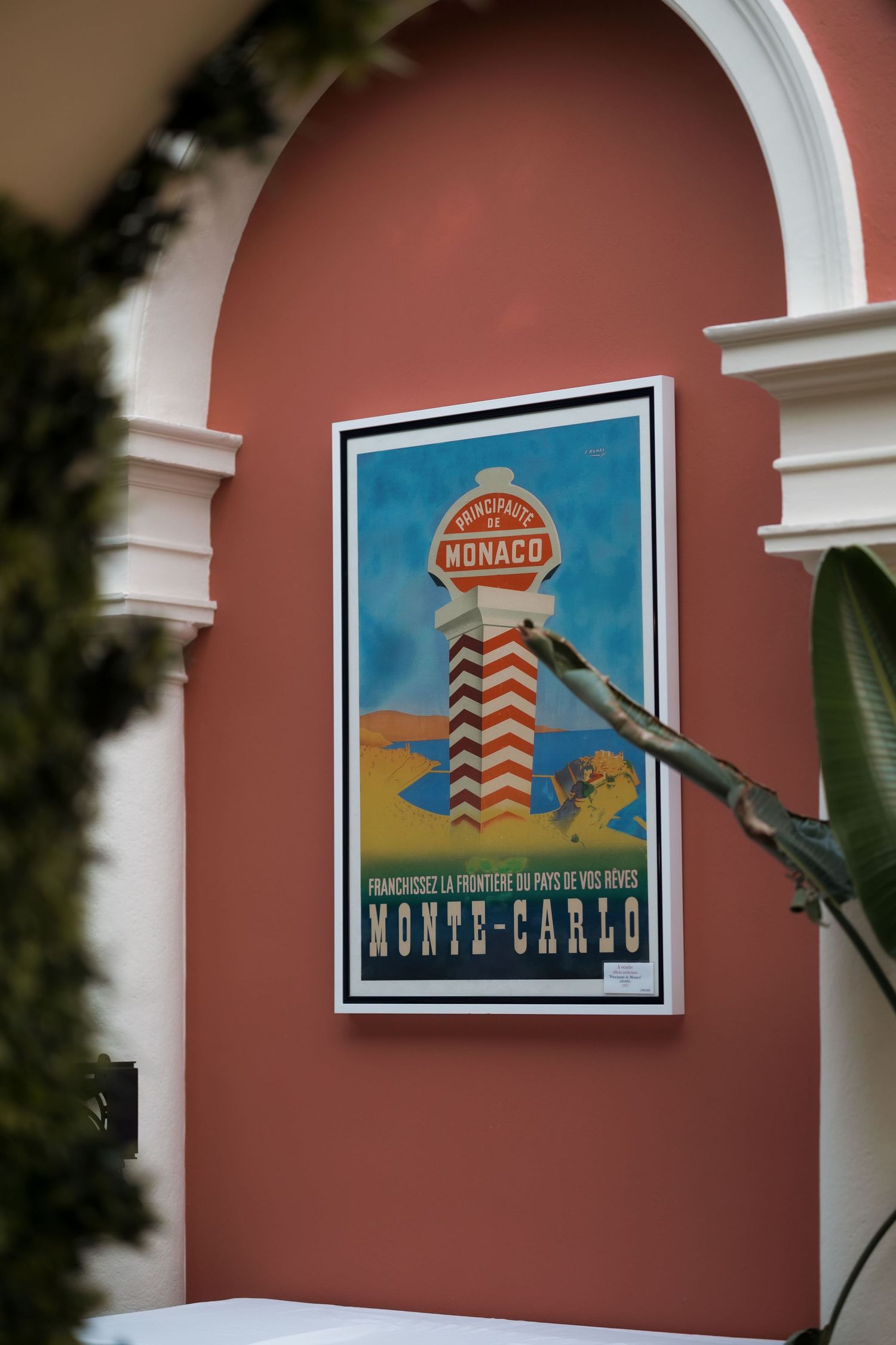 Vintage Monte-Carlo Monaco travel poster displayed on a terracotta wall beneath a white arch.