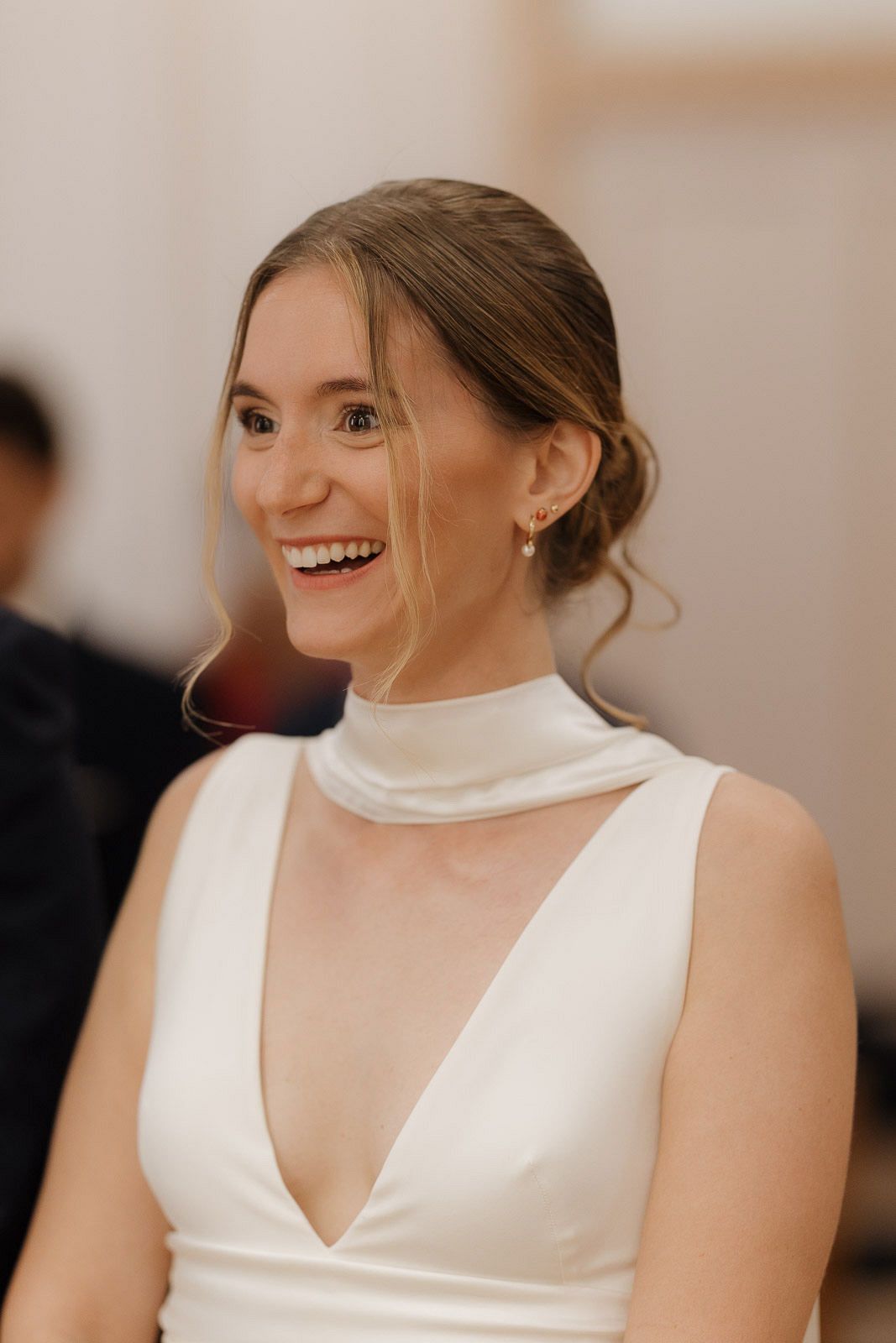 A bride in a sleeveless white wedding dress smiles joyfully during her wedding celebration.