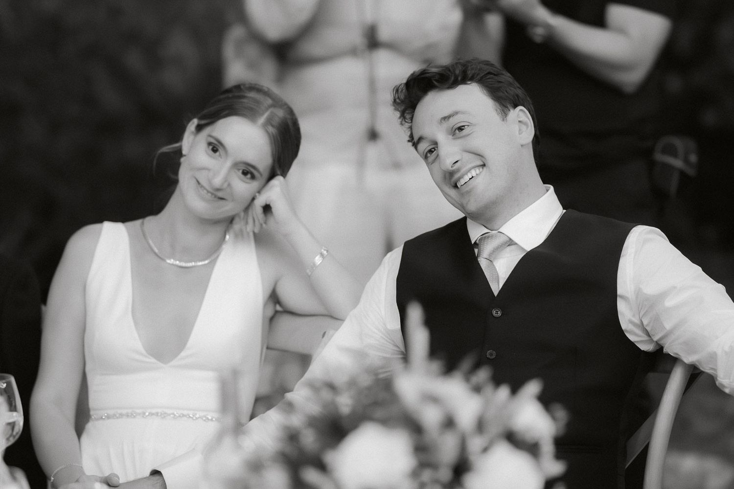 Black and white photo of guests seated at a wedding reception table during dinner.