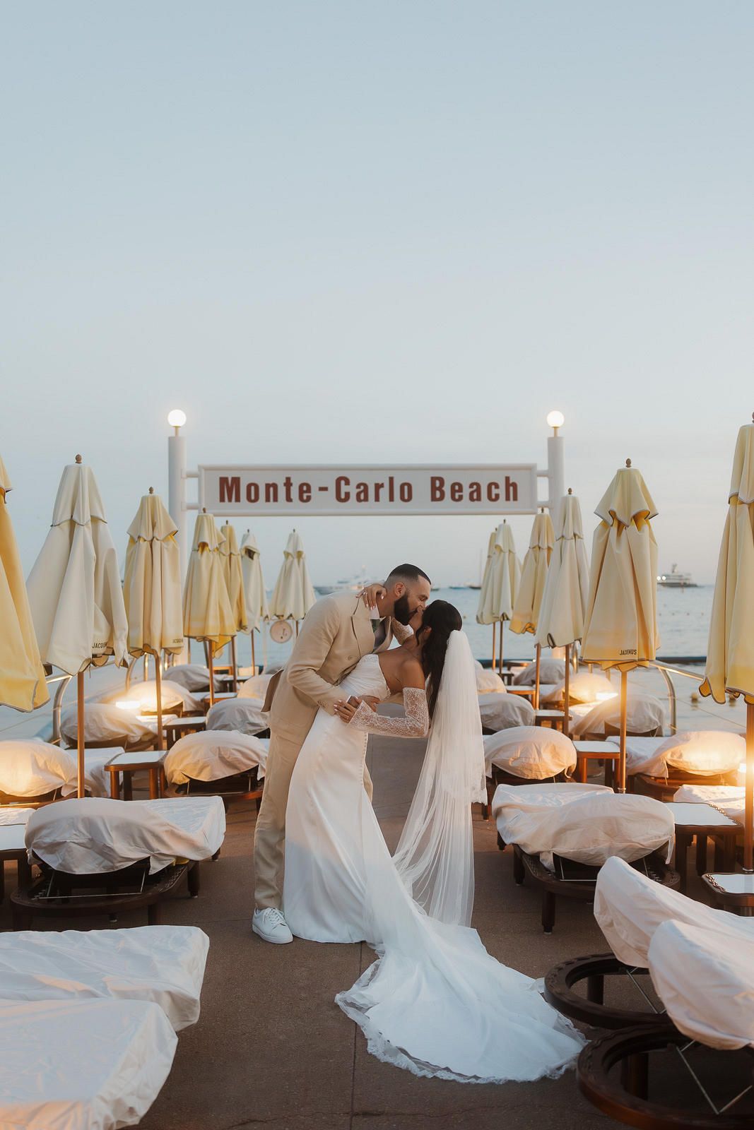 A row of white beach umbrellas and lounge chairs at Monte Carlo Beach at sunset creating a peaceful coastal scene.