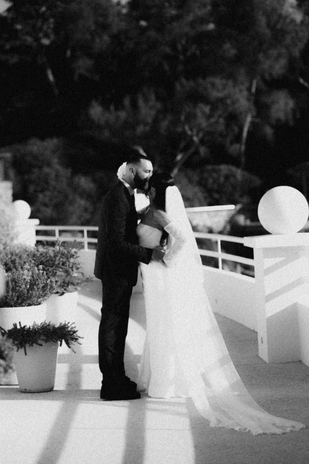A romantic black and white wedding photo of a couple sharing an intimate moment on an outdoor terrace.