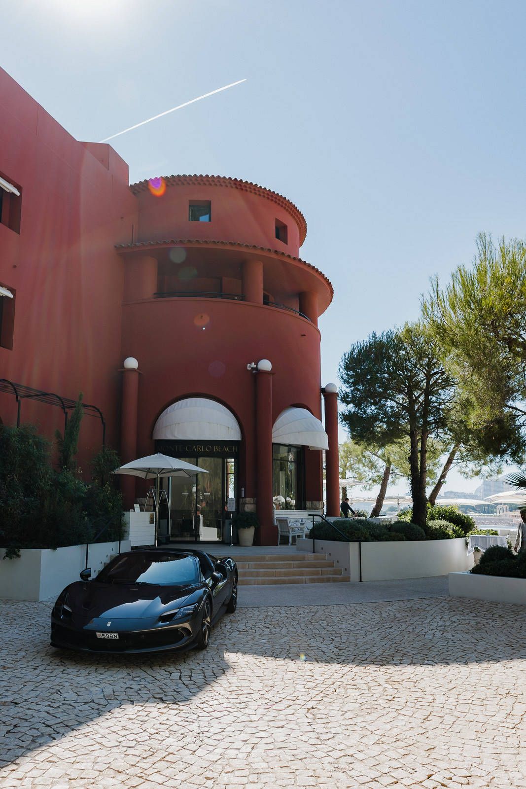 A sleek black sports car parked in front of a curved terracotta-colored building with white stone pavement.