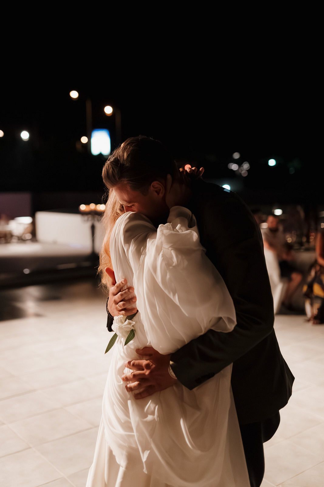 Couple shares an intimate dance moment under twinkling lights at their evening wedding reception.