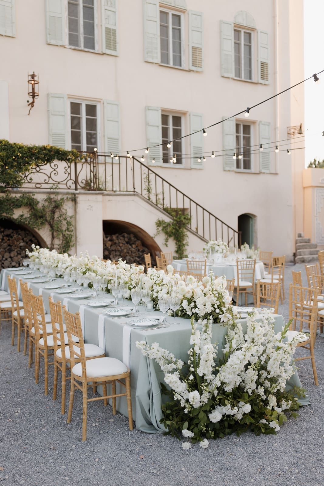 Elegant outdoor wedding reception setup with long tables draped in light blue linens and white floral arrangements.