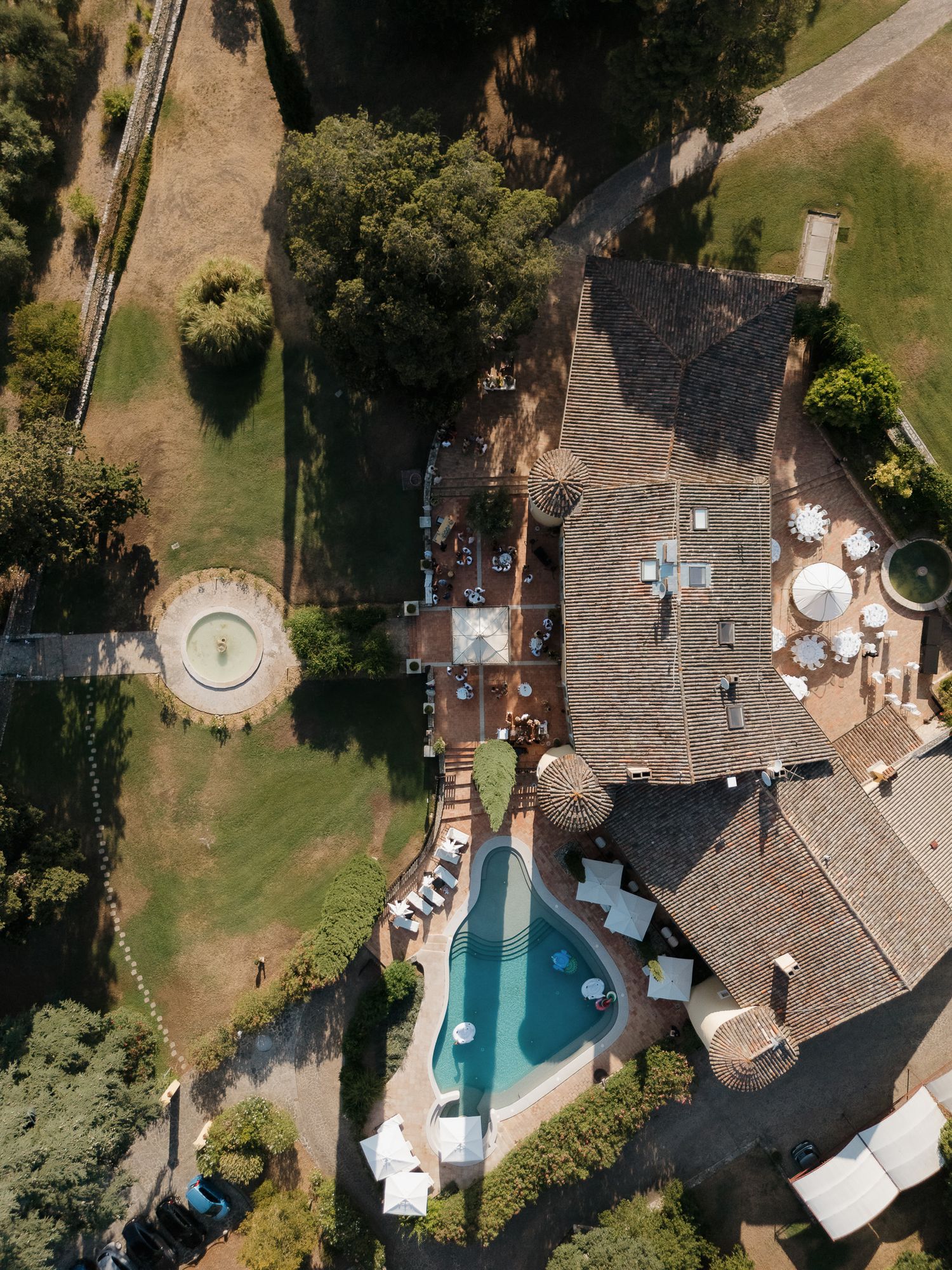 Aerial drone view of a luxury villa with a pool, terracotta roof, and lush gardens.