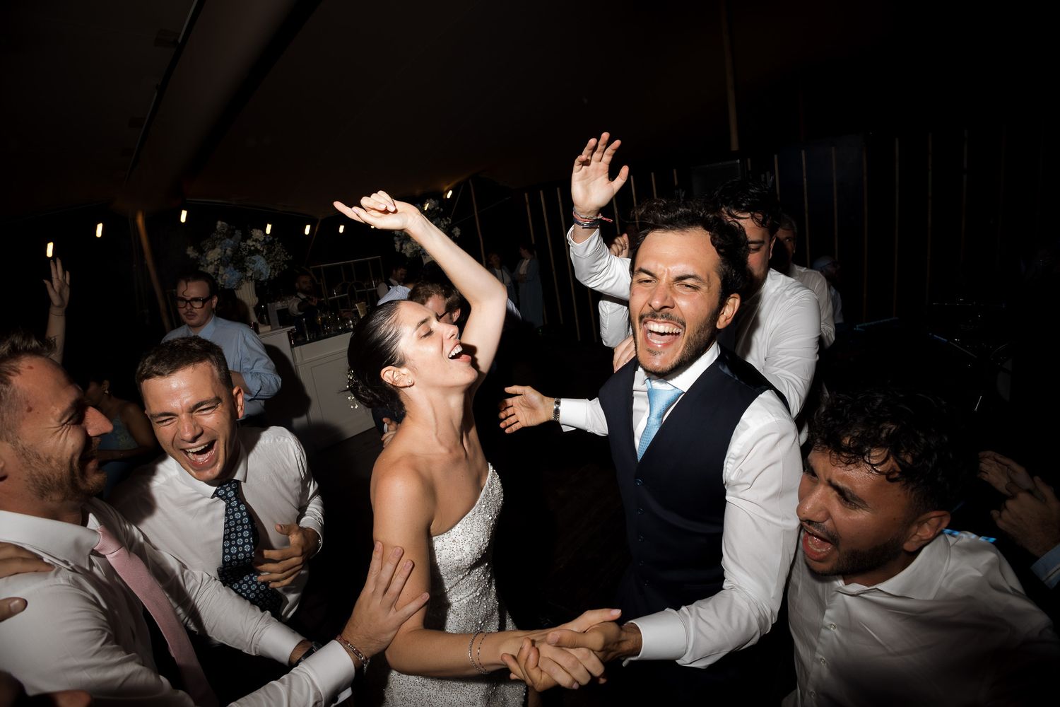 Joyful bride and groom dancing with guests at a lively wedding reception celebration.