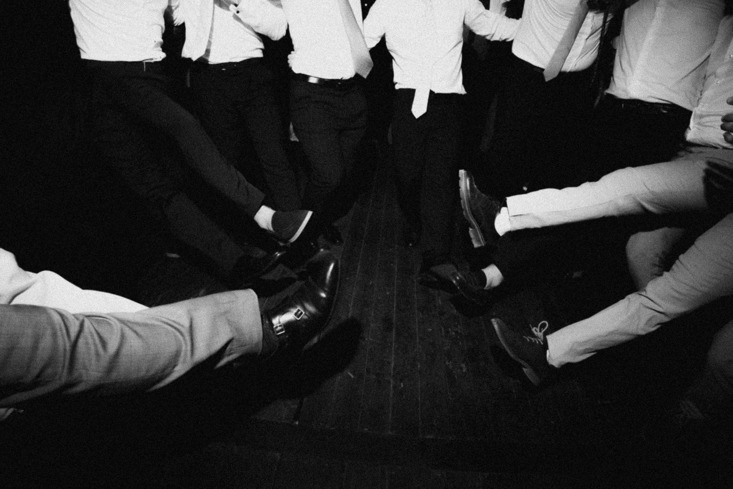 Black and white photo of a group of men in formal attire, focusing on their dress shoes gathered in a circle.