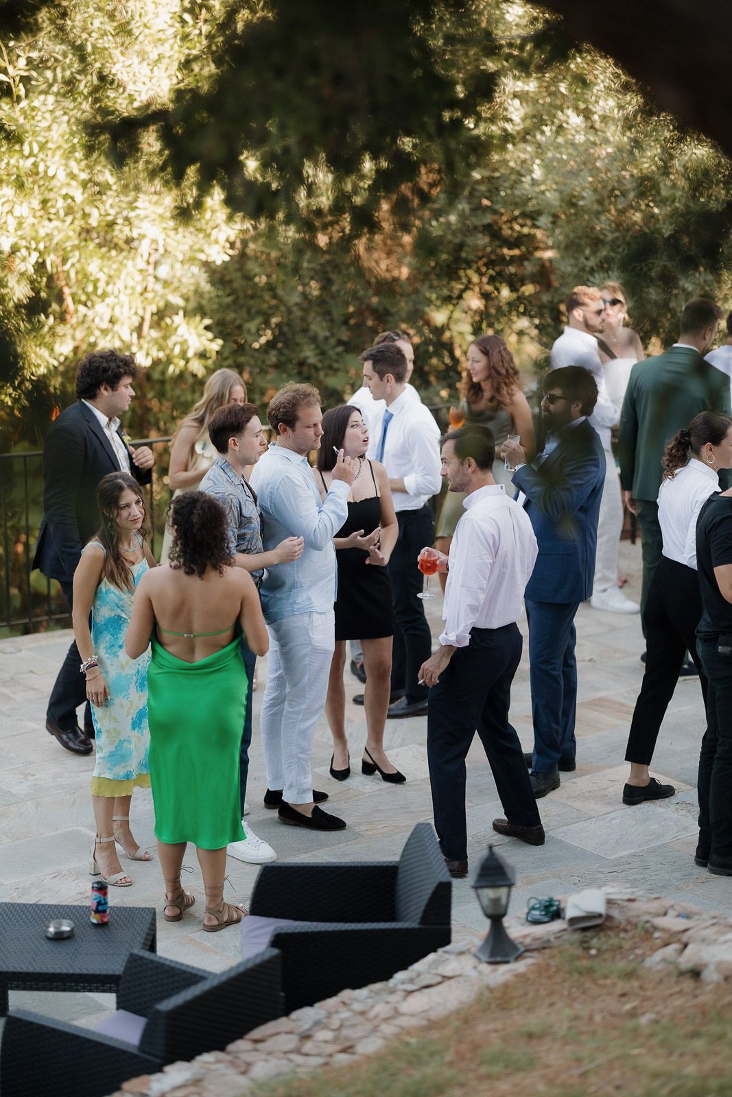 Wedding guests mingle and dance at an outdoor reception with trees in the background.