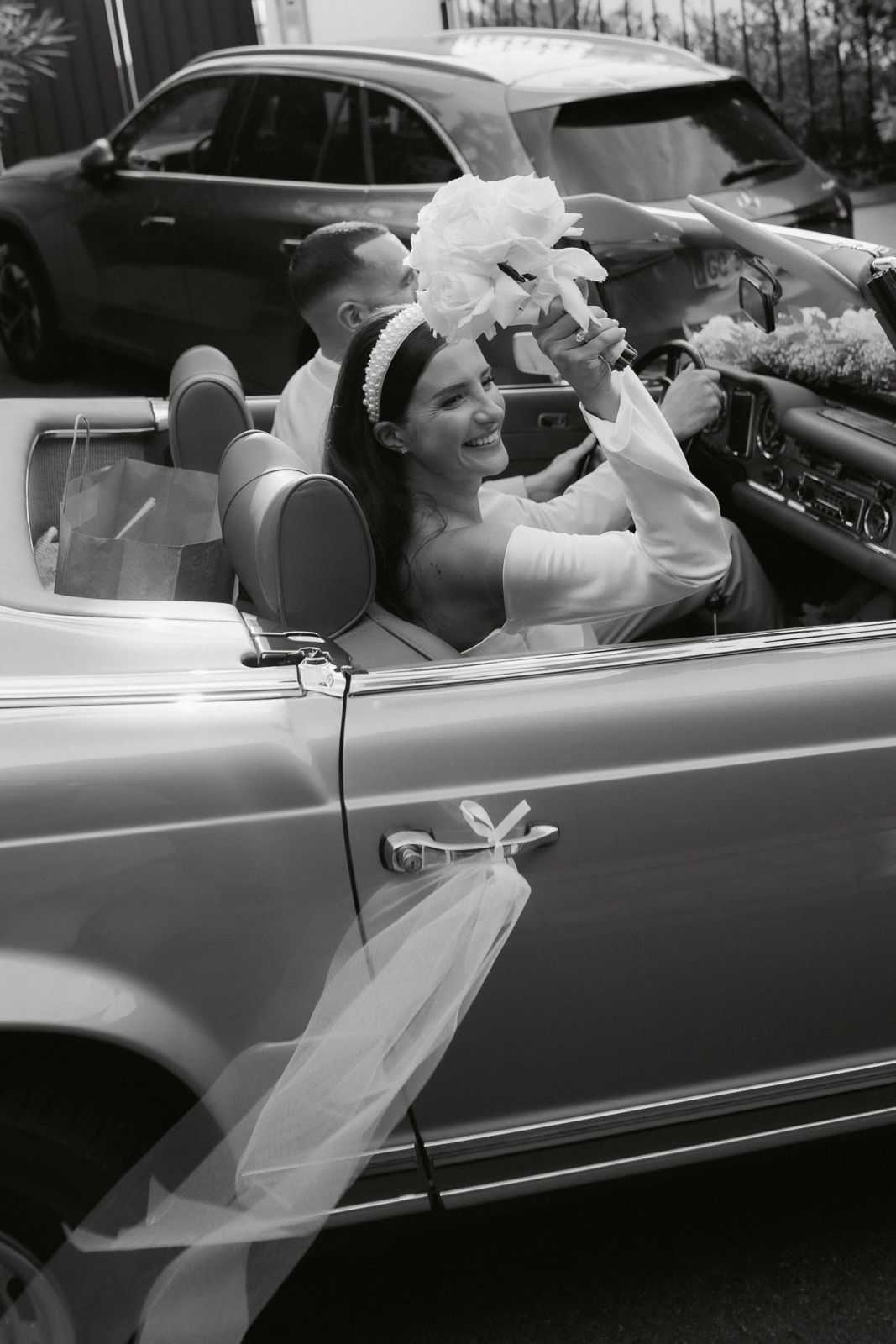 A sequence of black and white photos showing a bride in a convertible car with a flowing veil on her wedding day.