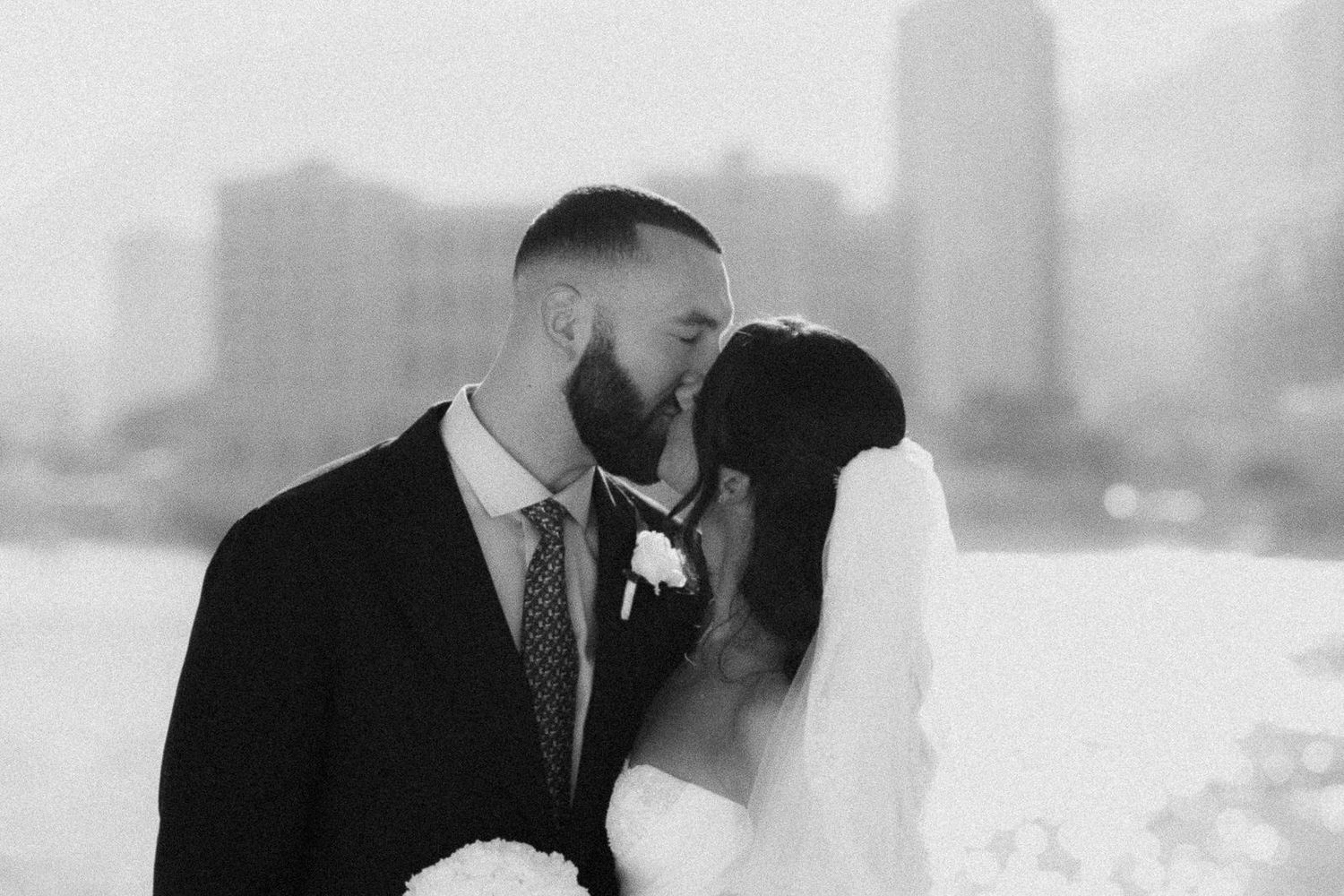 Black and white cityscape wedding photo showing urban skyline in soft focus.
