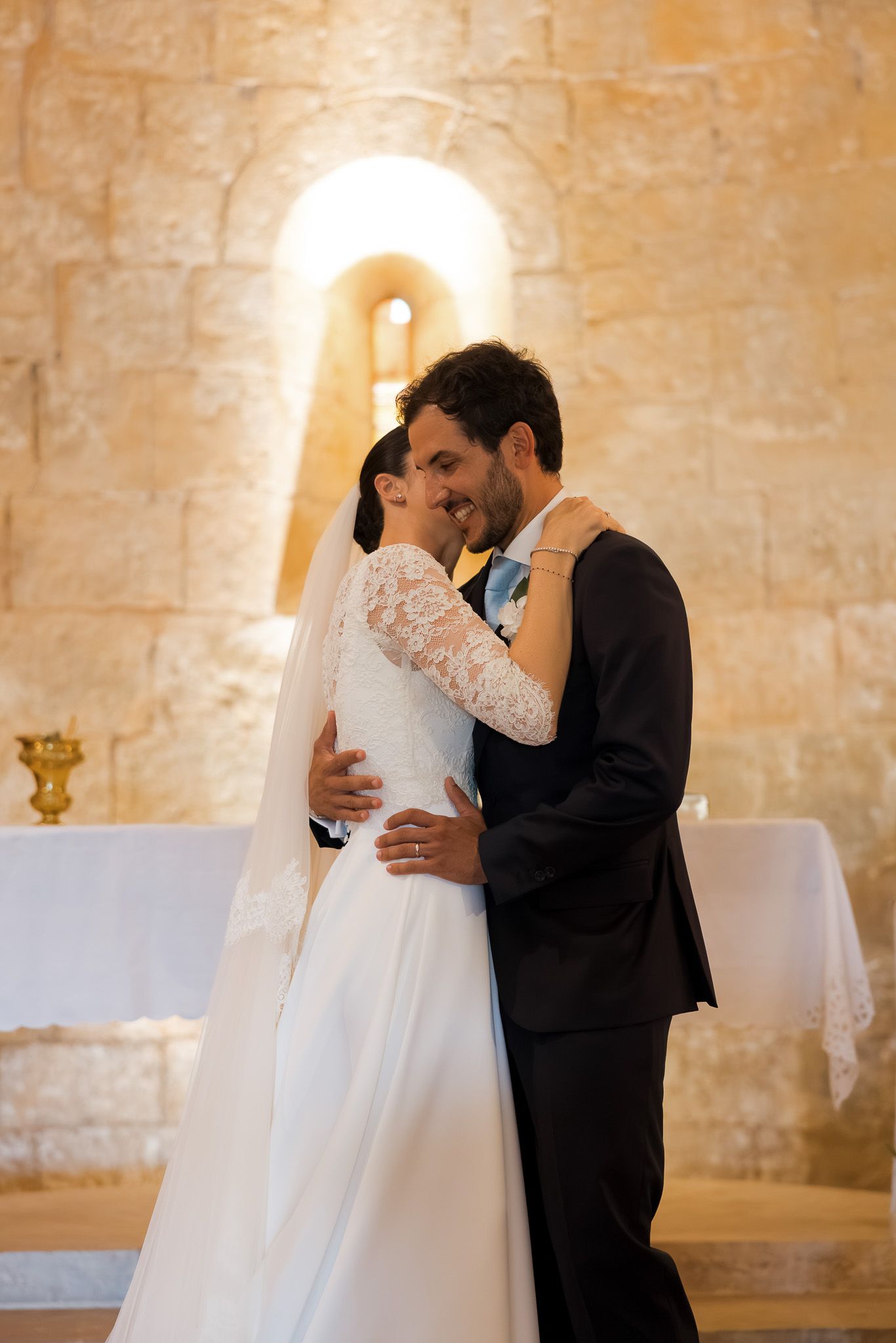 Bride and groom share first kiss at altar in rustic stone church during wedding ceremony.