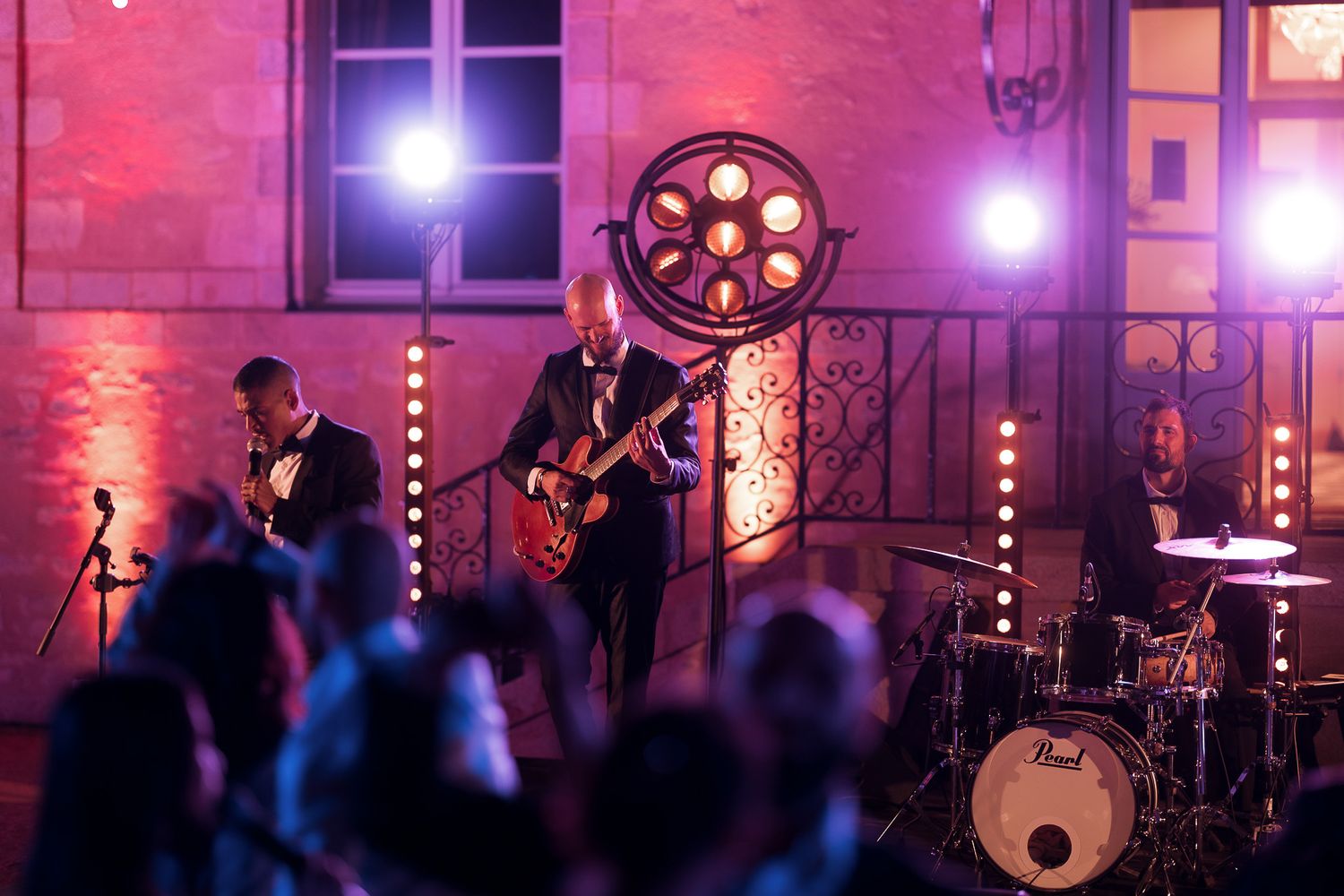 Live band performing outdoors at night with guitar, drums, and stage lighting at an elegant venue.