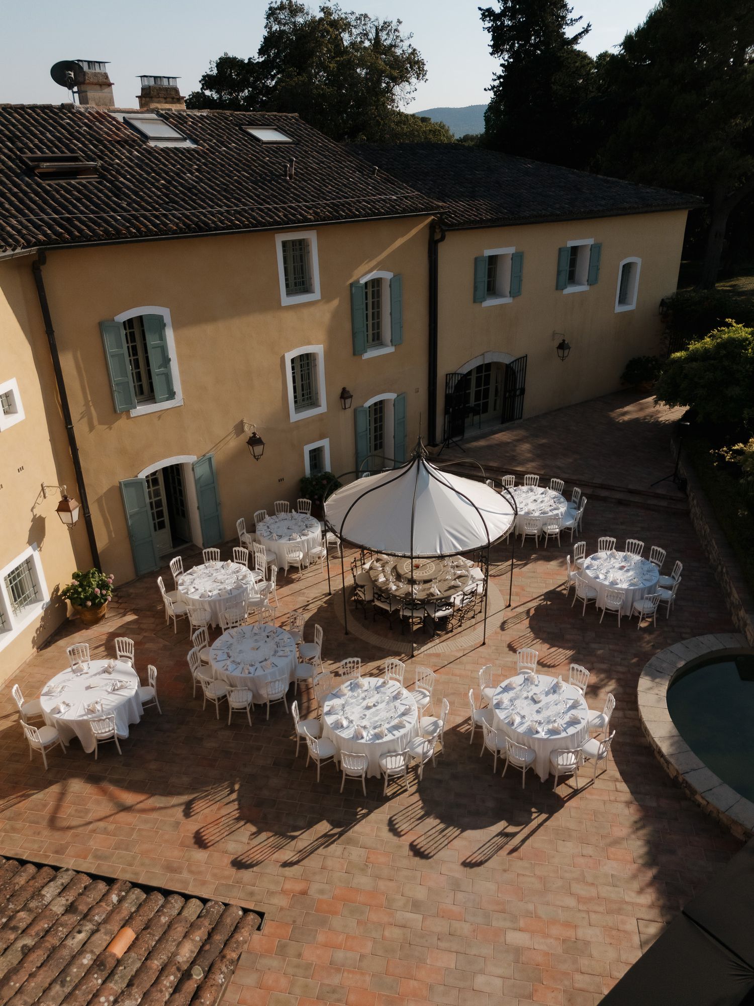 Aerial view of an elegant outdoor wedding reception setup in a courtyard of a yellow Tuscan villa with white-draped tables.