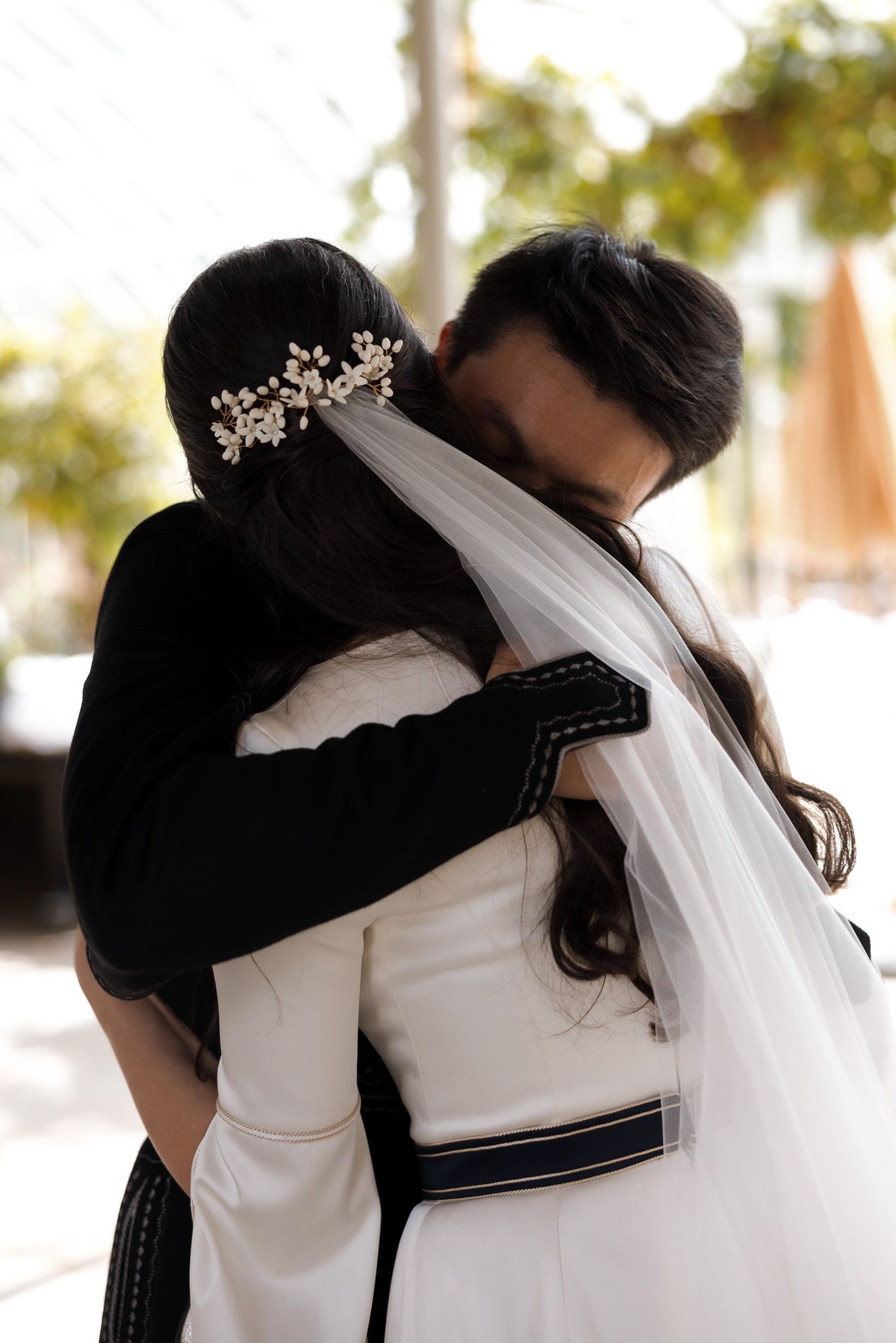 Bride and groom share an emotional embrace, bride wearing white gown with veil and floral hair accessory.