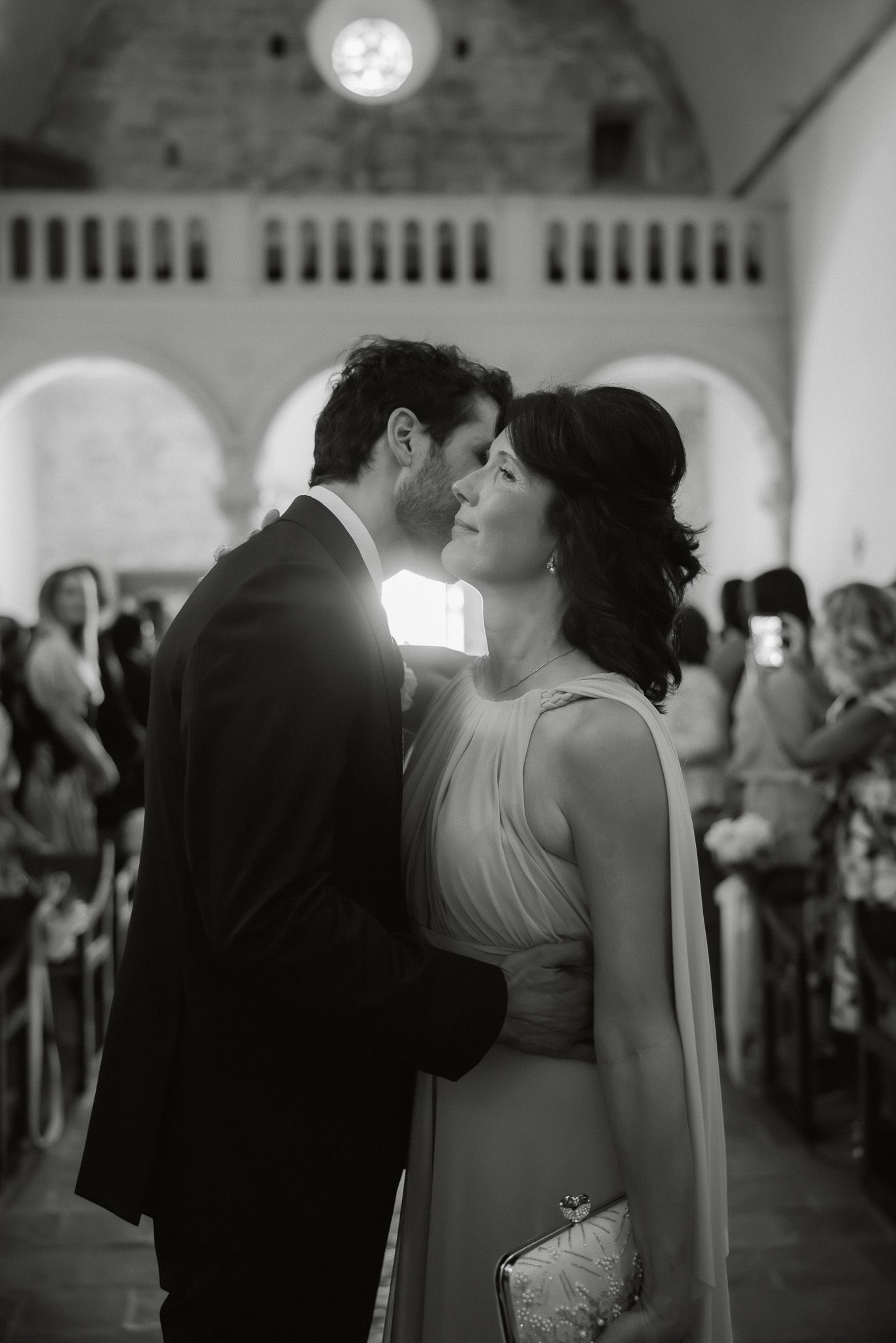 Black and white photo of a couple sharing a romantic moment at a wedding ceremony in an elegant venue.