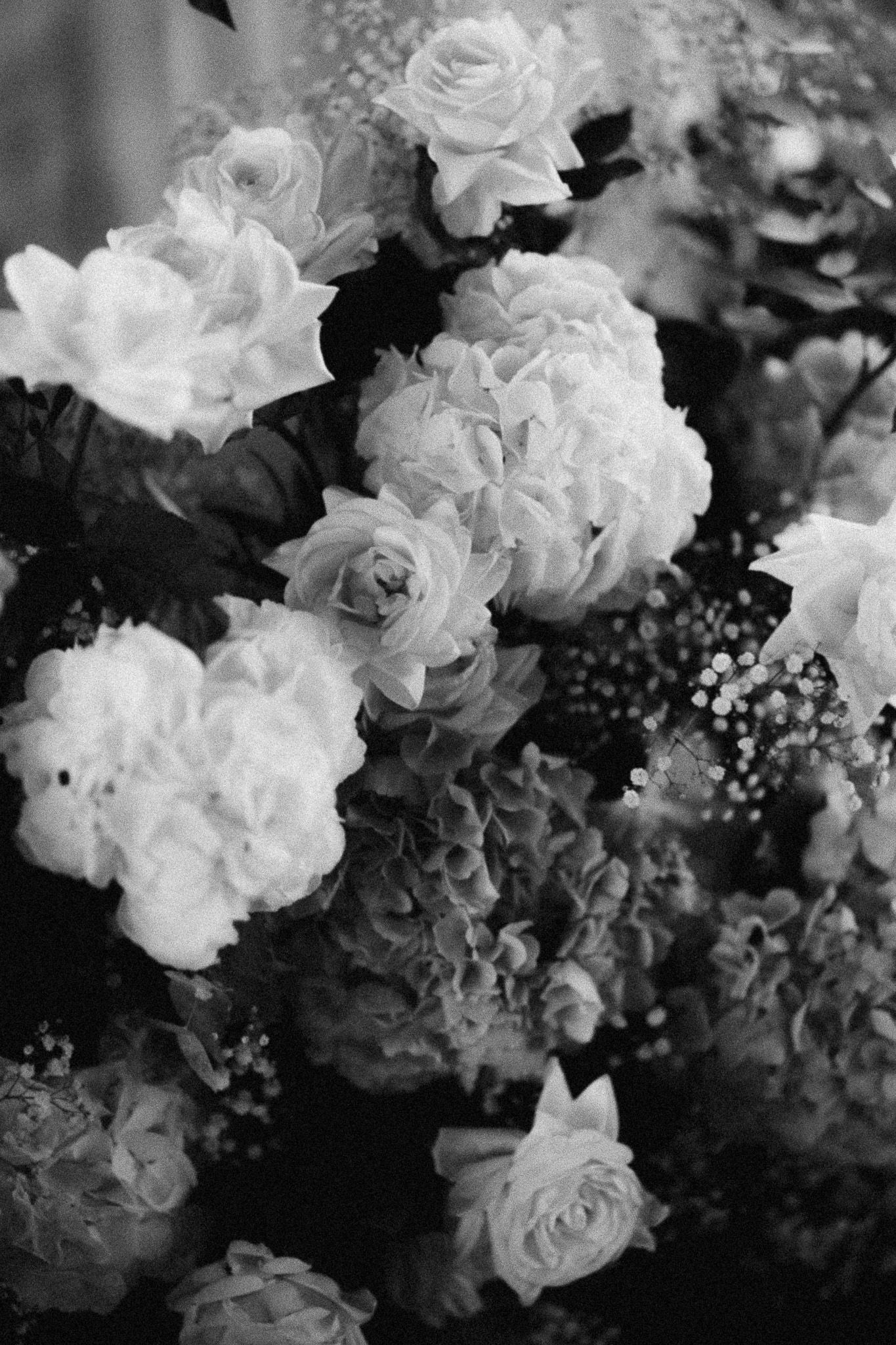 Black and white photo of a lush floral arrangement featuring roses, hydrangeas, and baby's breath in full bloom.