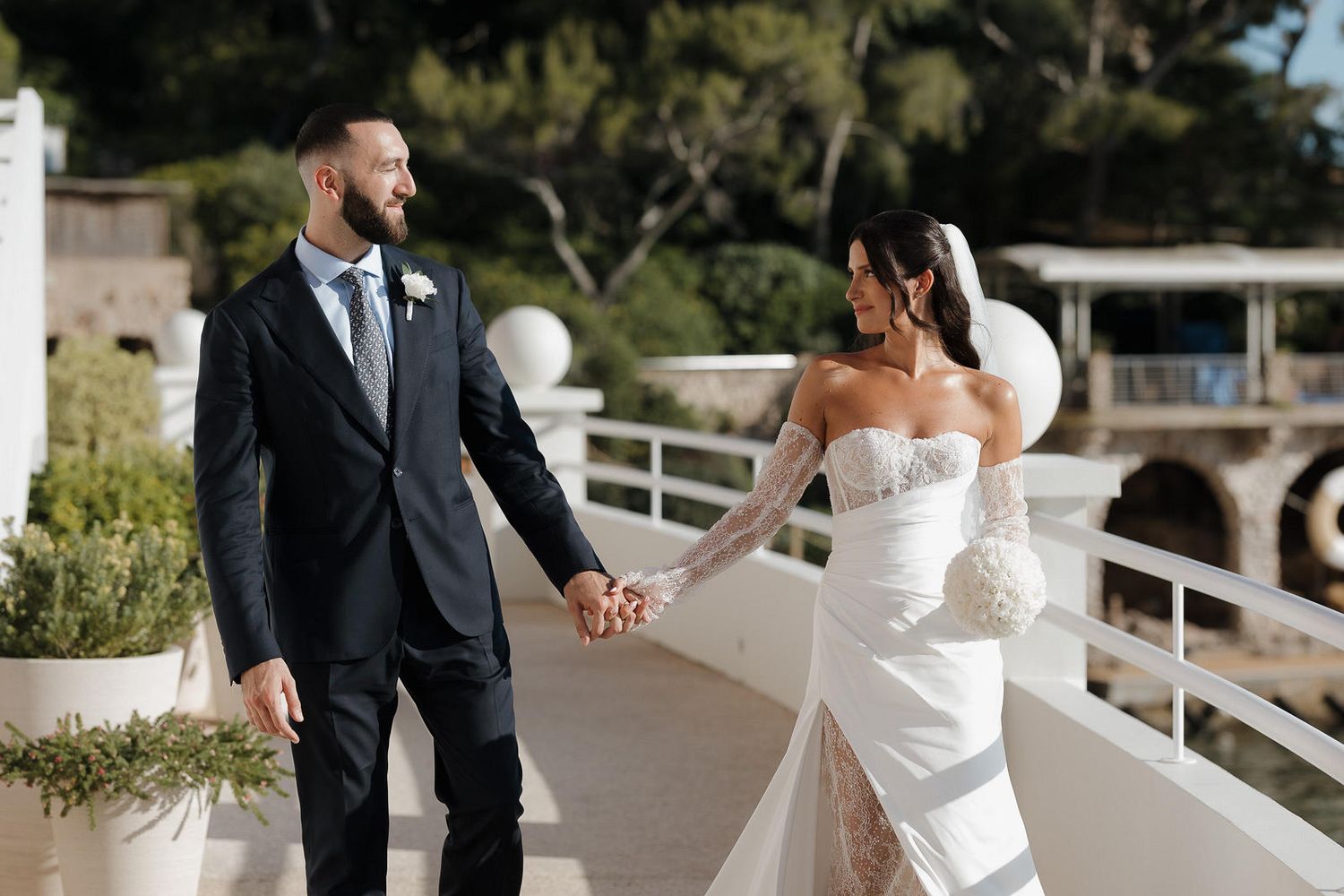 A couple in formal wedding attire dance together outdoors at their wedding celebration.