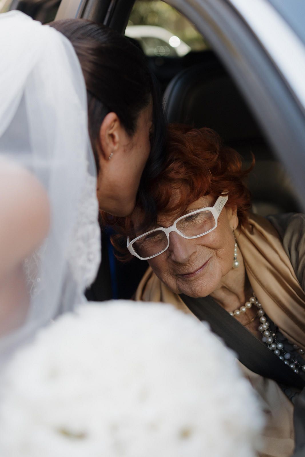 A person wearing glasses and a beige jacket sits in a car looking down.
