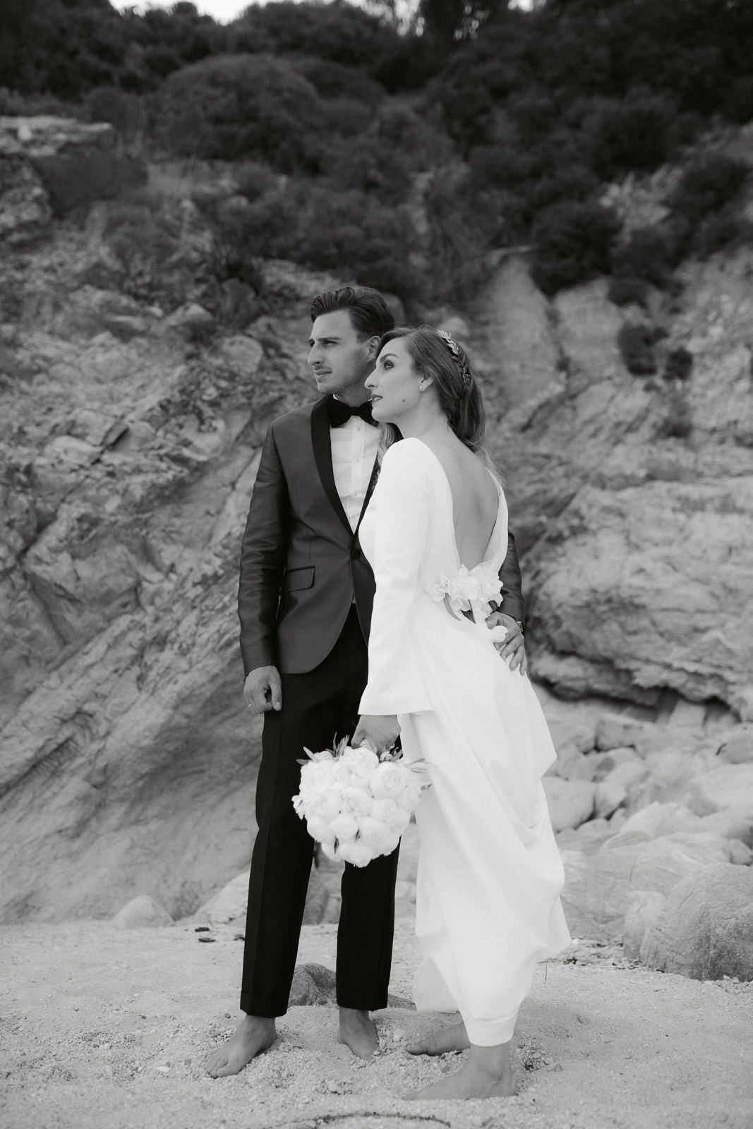 A romantic black and white wedding photo series showing a couple embracing on a rocky beach landscape.