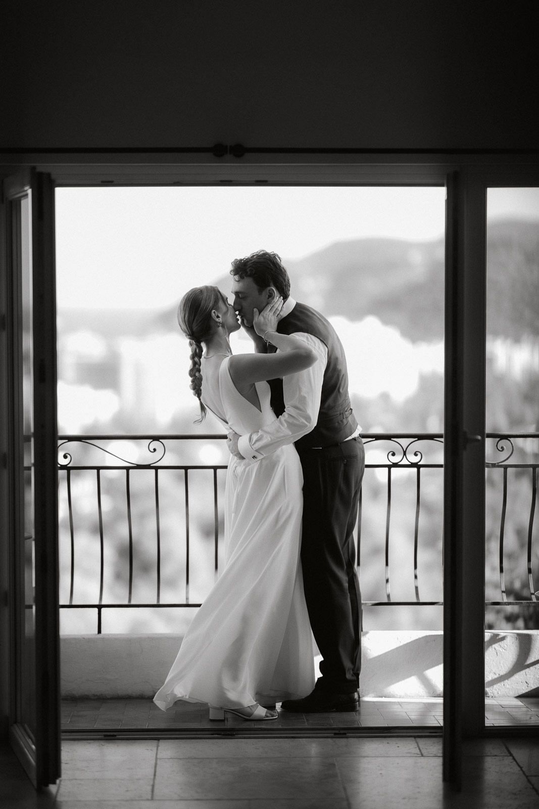 A romantic black and white photograph of a couple sharing an intimate moment on a balcony overlooking a scenic view.