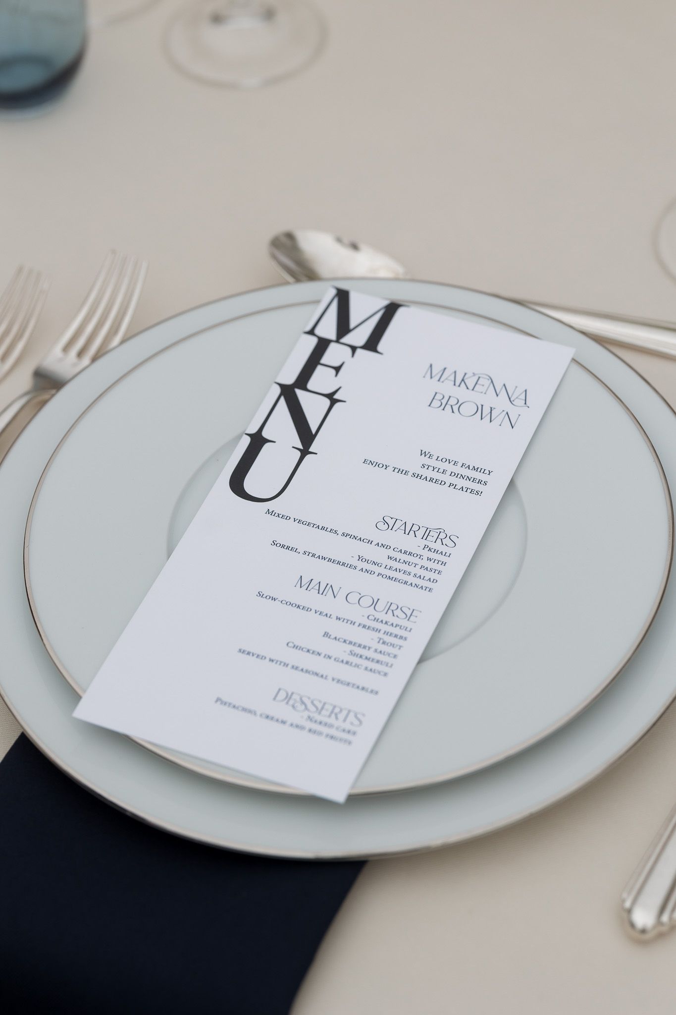 Elegant wedding place setting with personalized menu card for Marenna Brown on white plate with navy napkin.