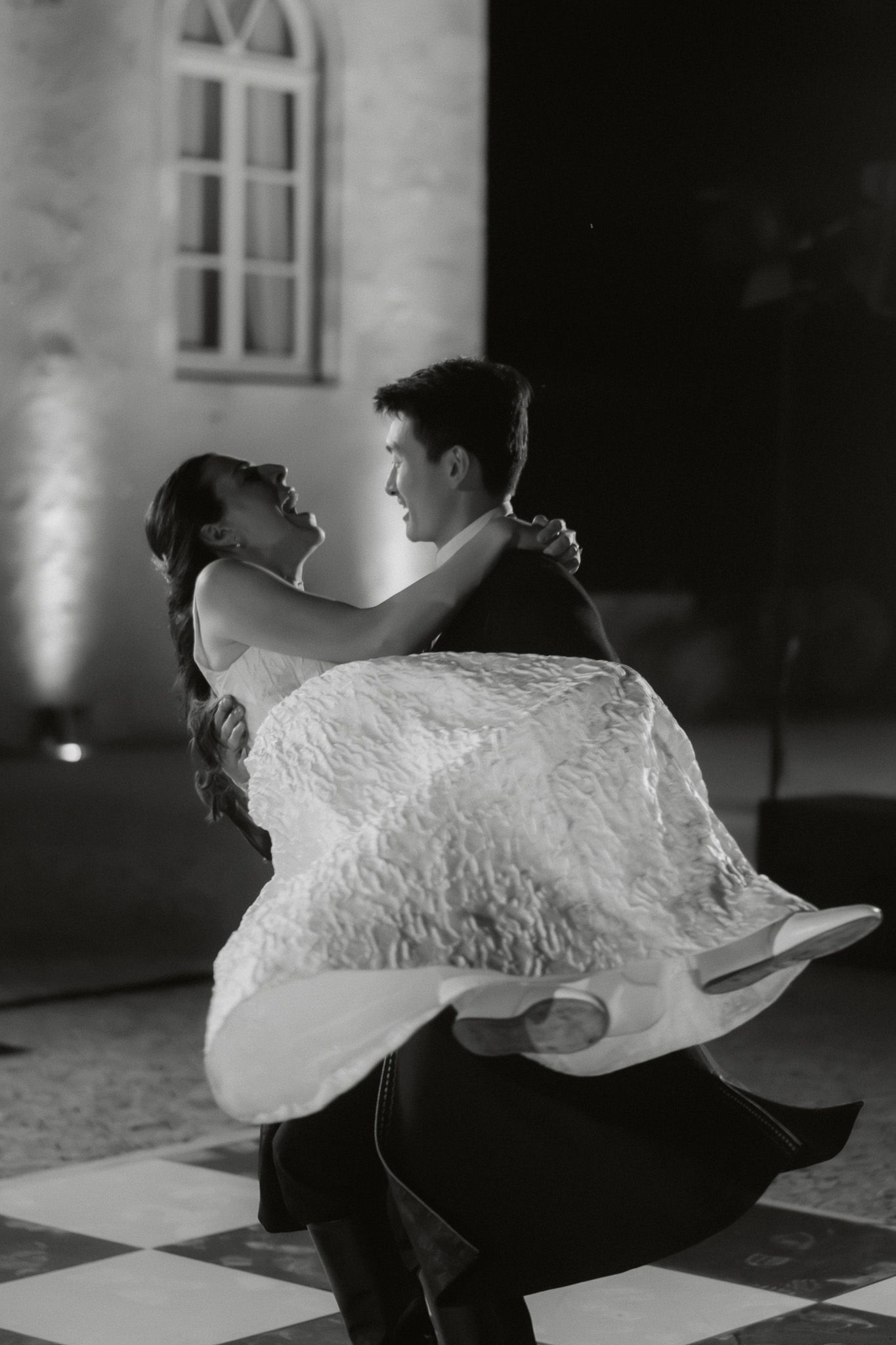 Black and white photo of a couple sharing their first dance at a wedding, bride in flowing gown, groom in tuxedo.