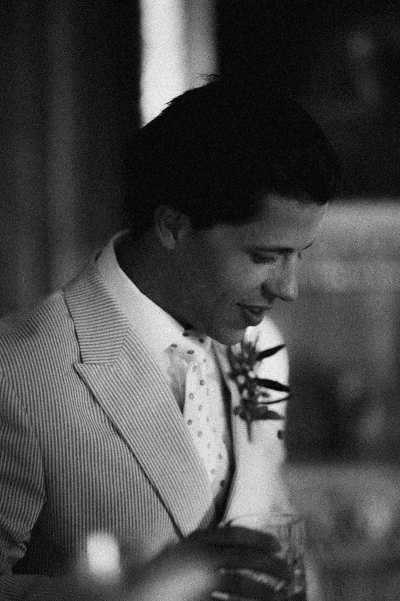 Black and white portrait of a smiling young man in a striped suit and dotted tie looking down elegantly.