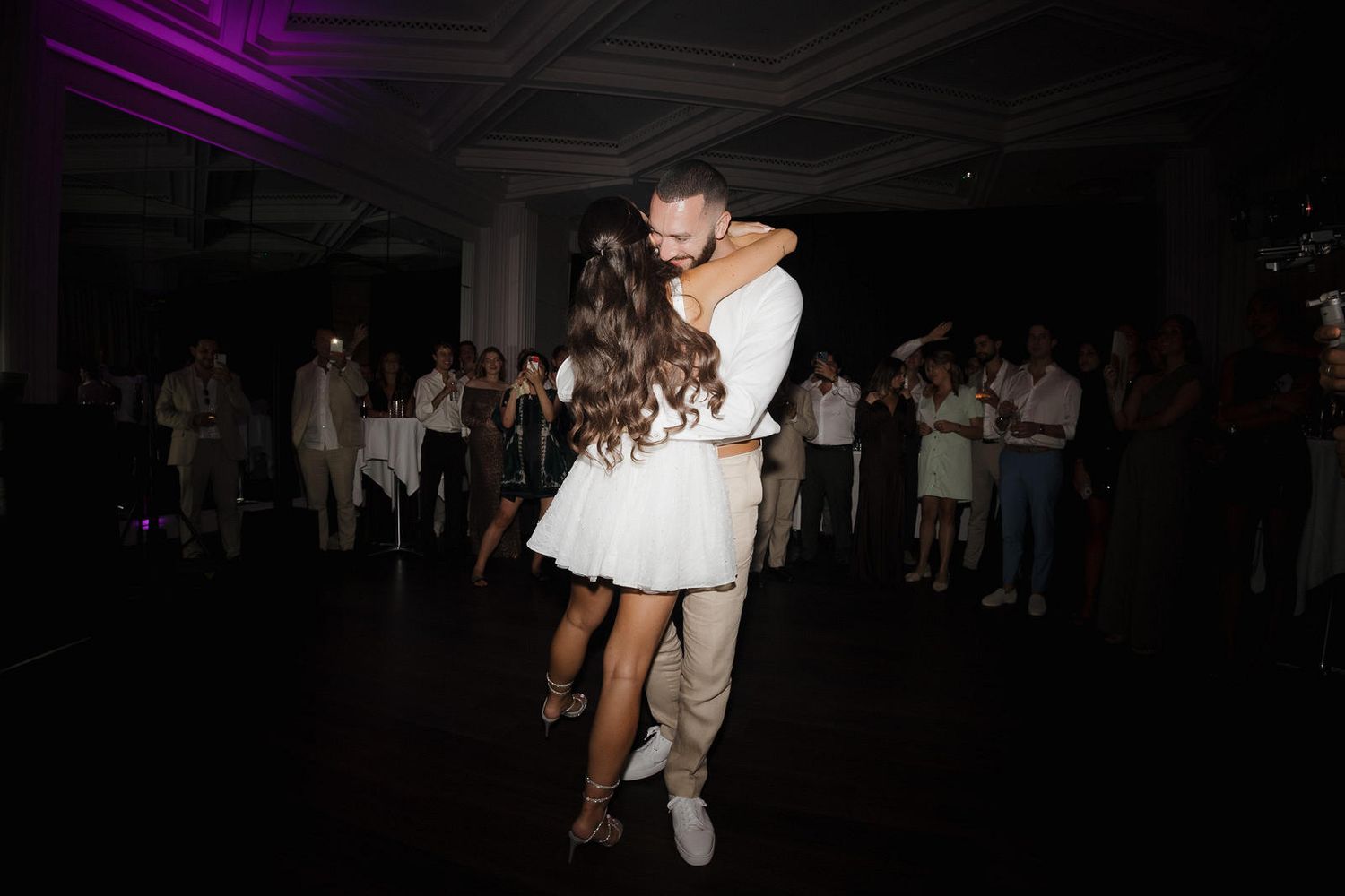 Wedding guests dance and celebrate on a dimly lit dance floor during an evening reception.