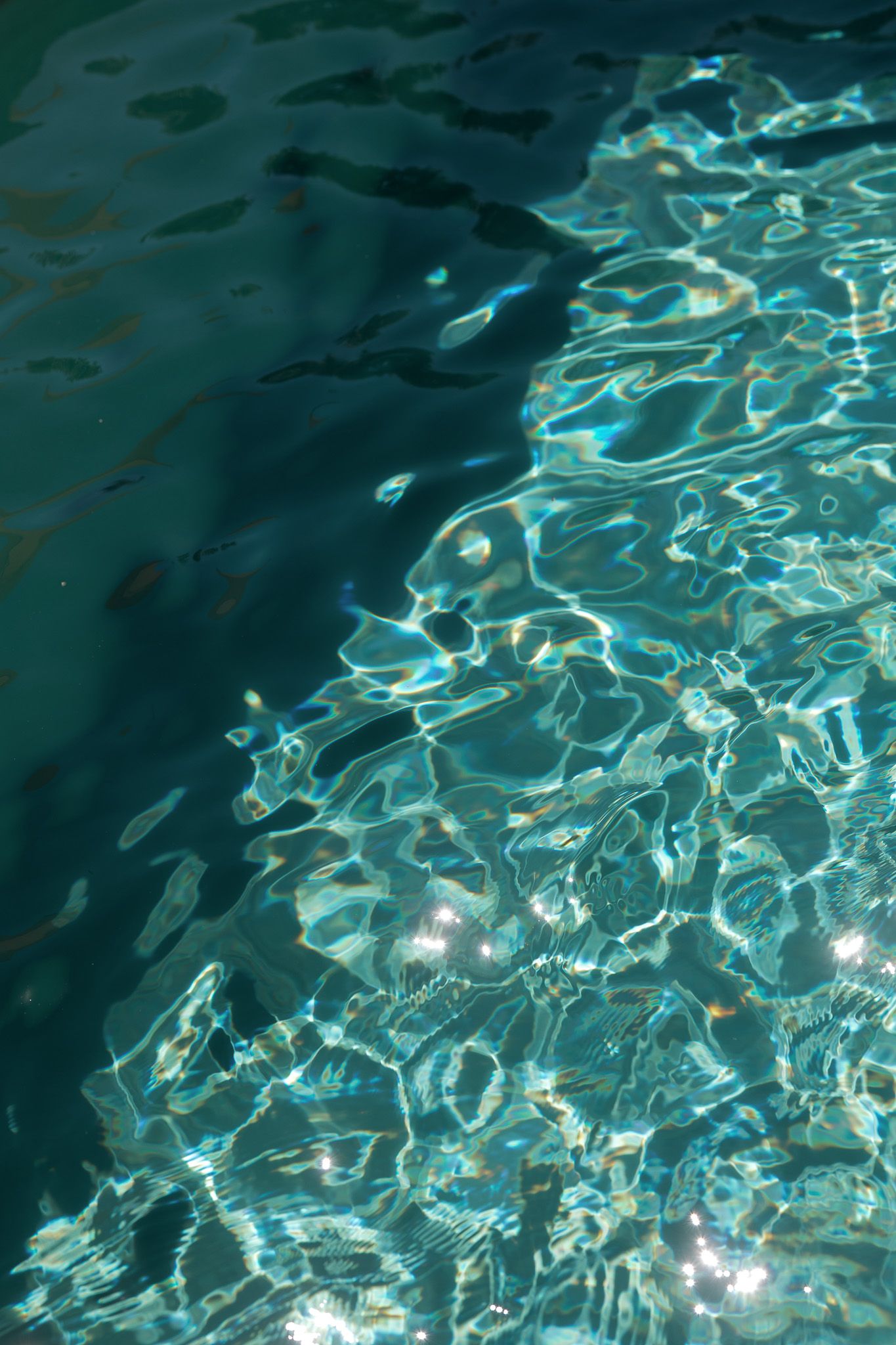 Sunlight shimmering on clear turquoise pool water creating beautiful caustic light patterns on the surface.