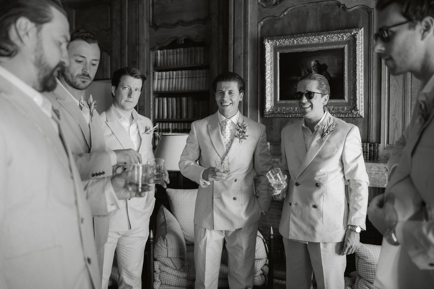 Black and white photo of groomsmen in light suits laughing and holding drinks at an elegant wedding reception.
