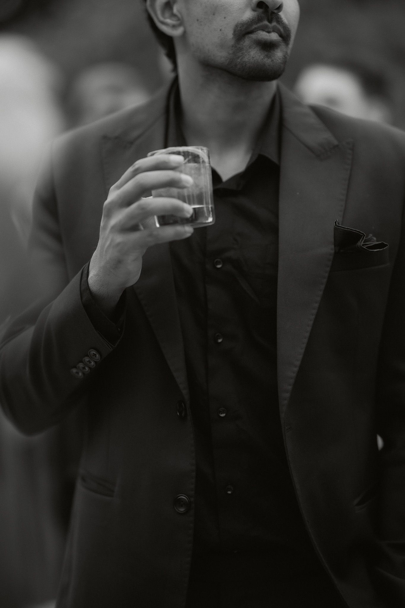 Black and white photo of a man in a suit holding a glass of whiskey at a formal event.