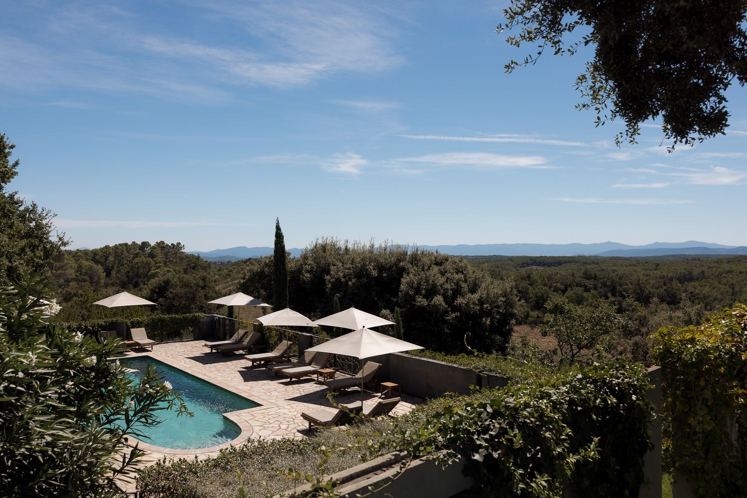 Luxury villa pool with sun loungers and umbrellas overlooking a scenic forested landscape under a clear blue sky.