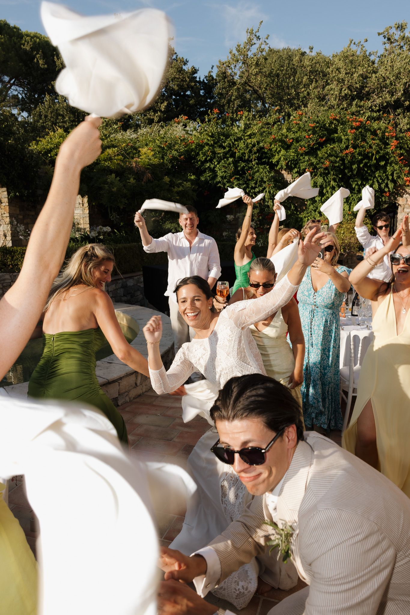 Joyful wedding guests waving white napkins celebrating with bride and groom outdoors.