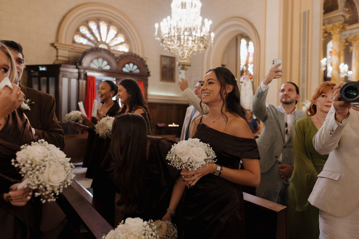 Wedding guests dancing and celebrating on a dance floor under elegant chandeliers at an indoor reception venue.