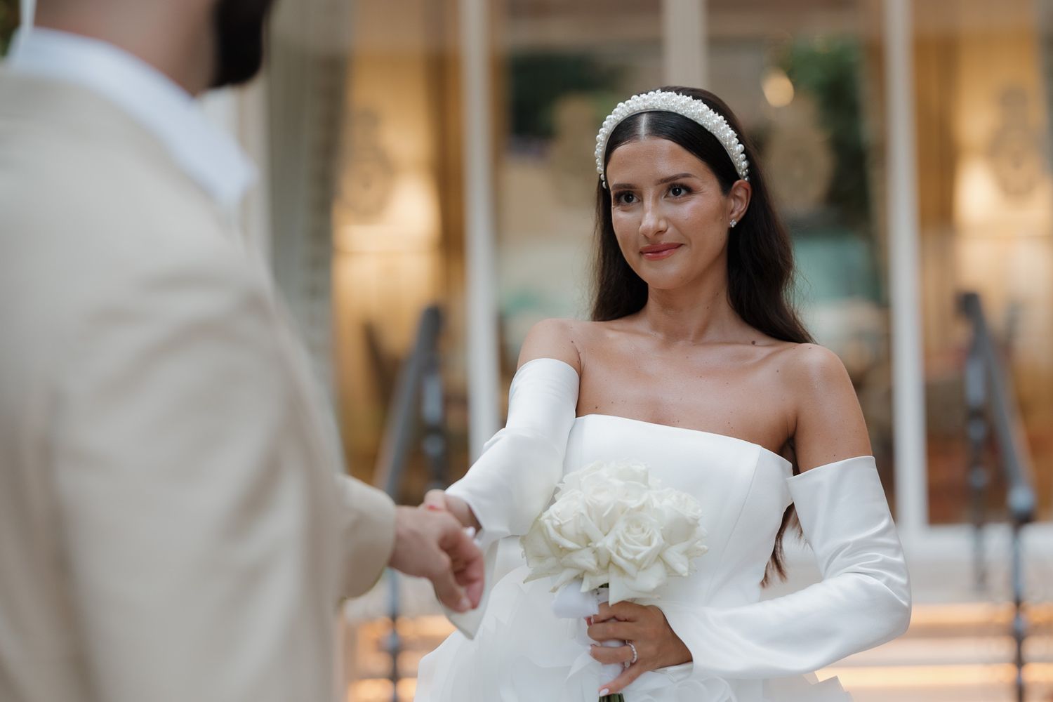 Bride in a strapless white wedding gown poses elegantly in an outdoor setting with soft natural lighting.