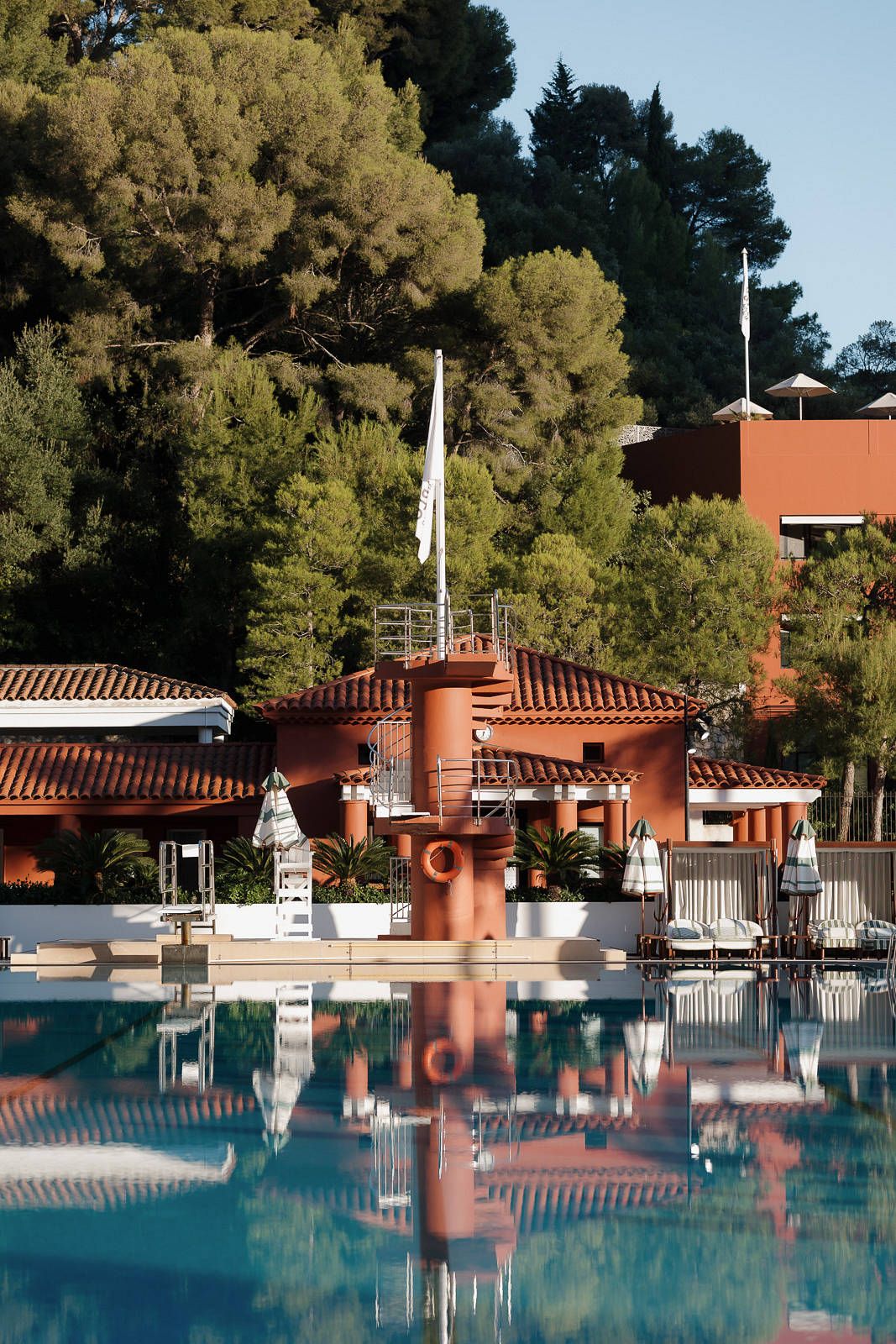 Serene swimming pool with terracotta columns and white accents reflecting in calm blue water at a luxury resort.