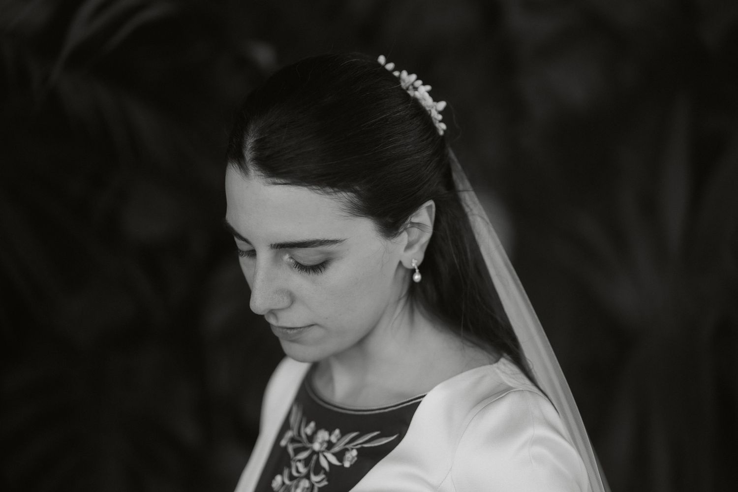 Black and white bridal portrait of a woman in a veil and floral headpiece looking down gracefully.