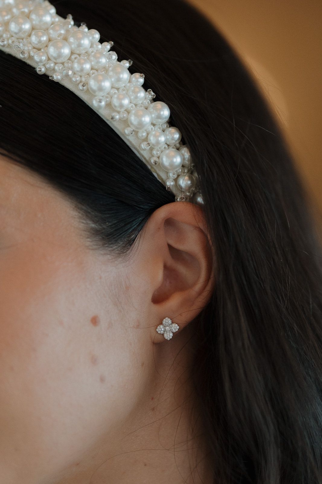 A delicate pearl headband adorns dark hair, with a small crystal earring visible in the ear.