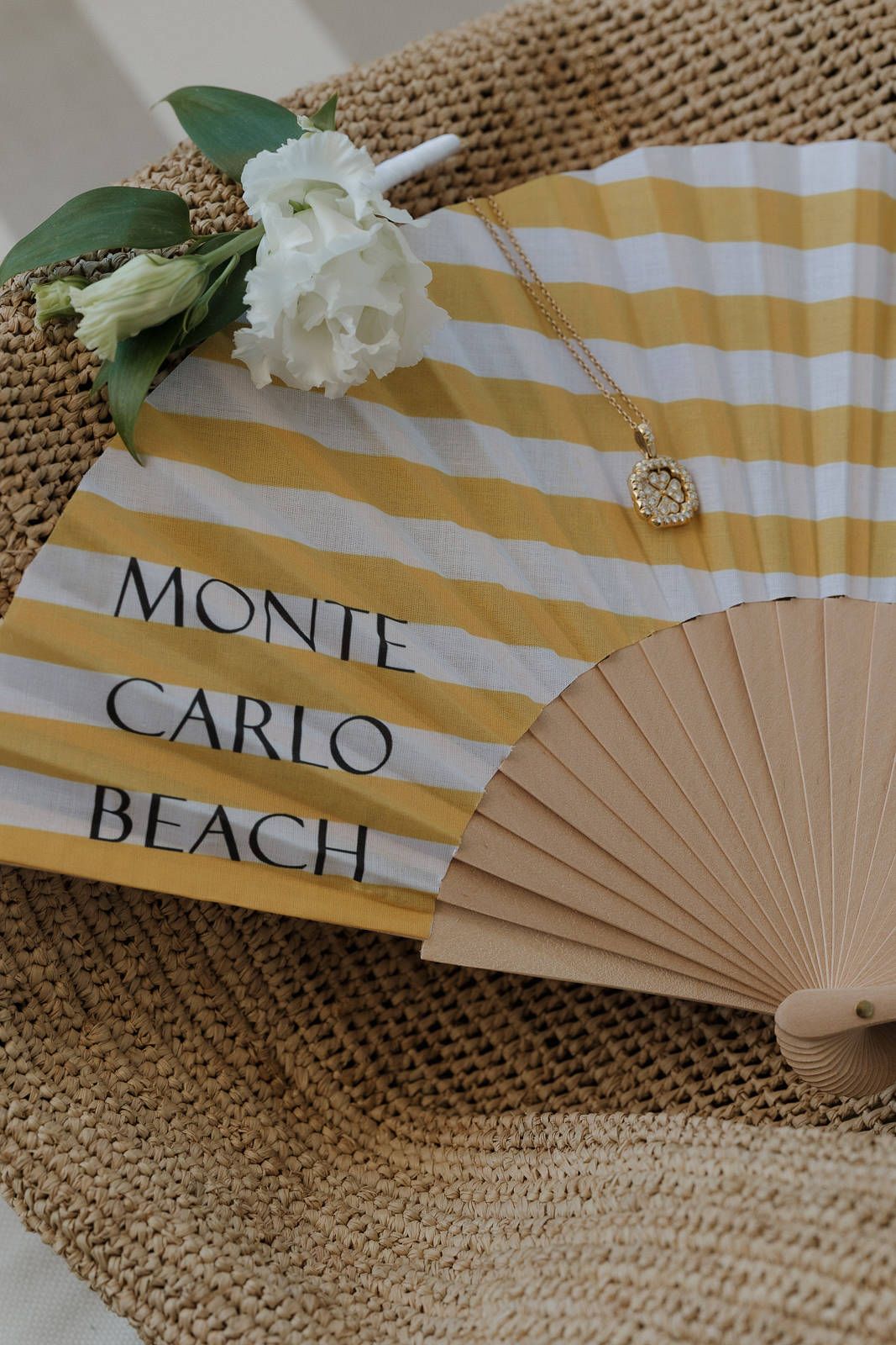 Decorative hand fans with Monte Carlo Beach text in yellow and white stripes lay on a textured burlap surface.