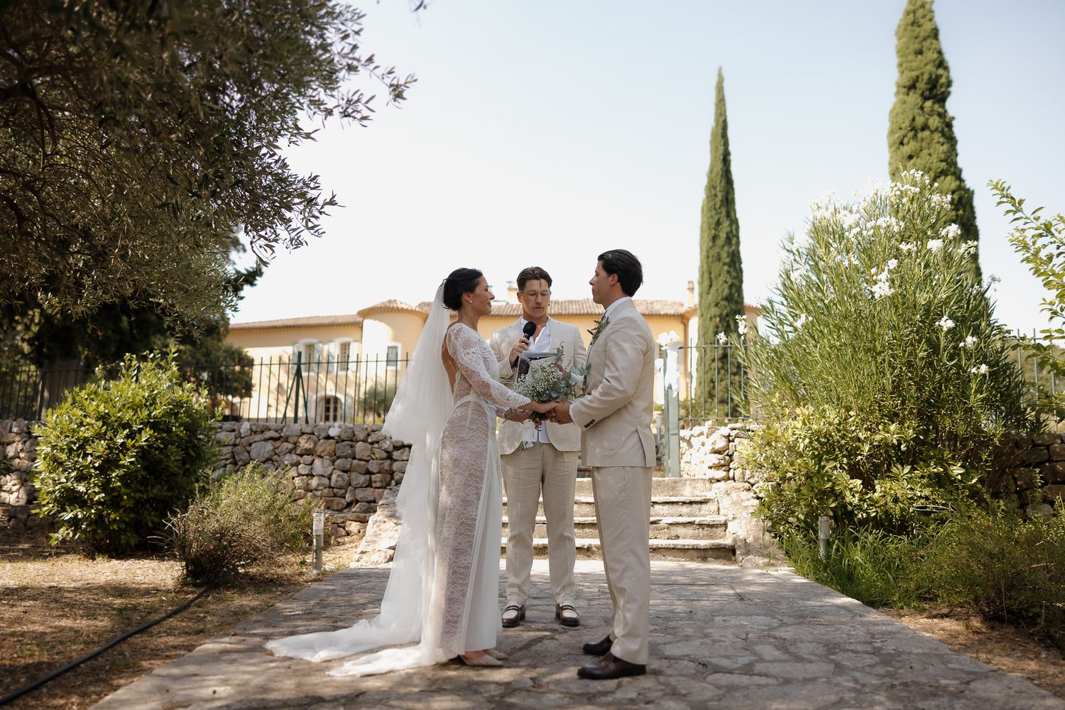 Bride and groom exchange vows with officiant outdoors at a Mediterranean villa wedding ceremony.