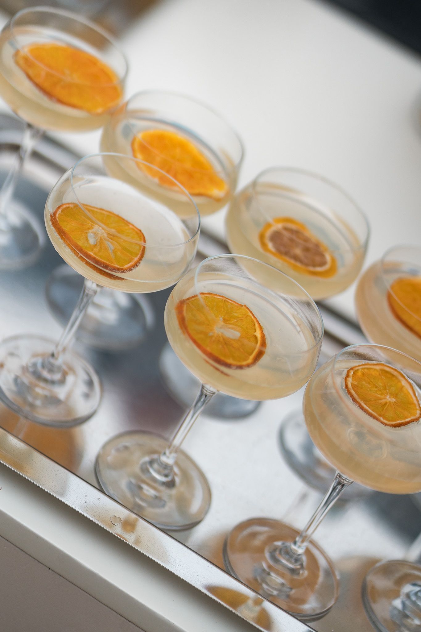 Elegant coupe glasses filled with champagne cocktails garnished with dried orange slices arranged on a silver tray.