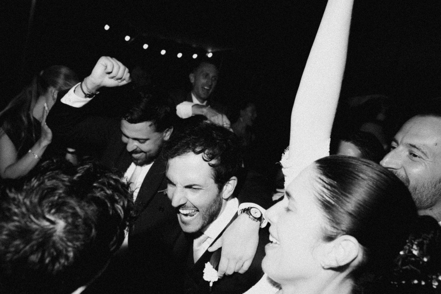 Black and white photo of joyful wedding guests dancing and celebrating at a lively wedding reception party.