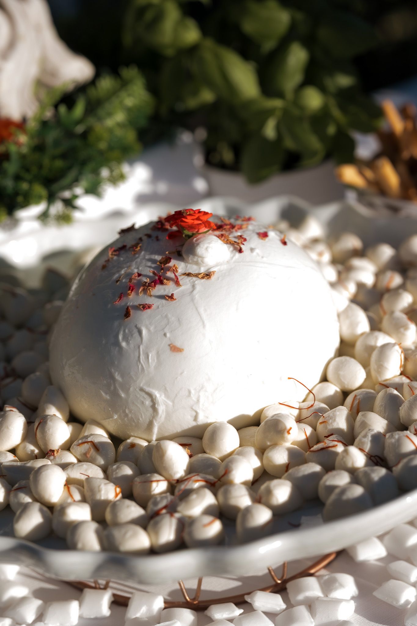 Fresh mozzarella ball topped with saffron threads on a bed of small white meringues on a glass plate.