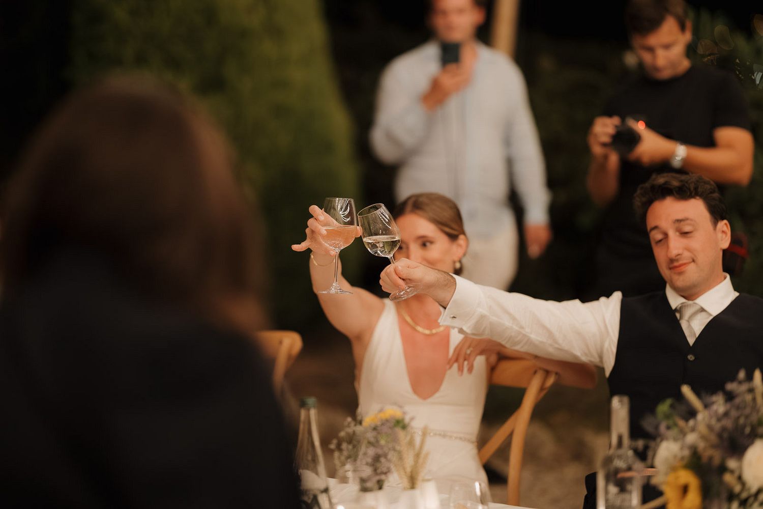 Wedding guests dancing and celebrating at an evening reception party with festive lighting and decorations.