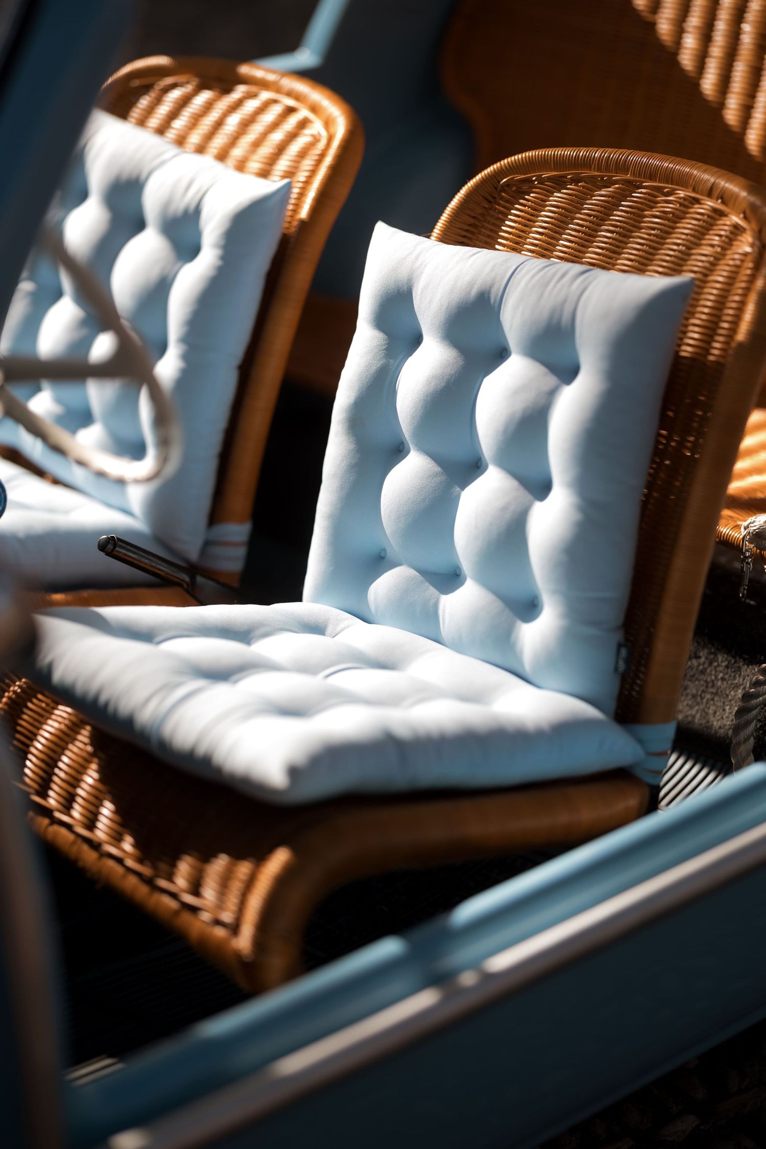 Wicker chairs with tufted white cushions in warm sunlight at an outdoor cafe.