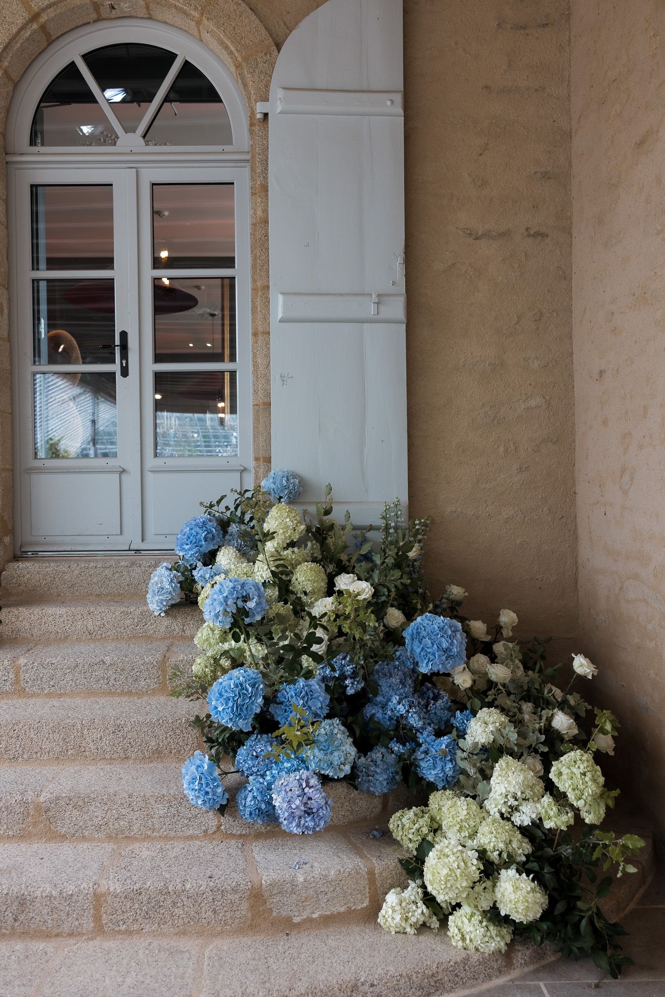 Blue and white hydrangea floral arrangements cascading down stone steps beside an elegant French door entrance.