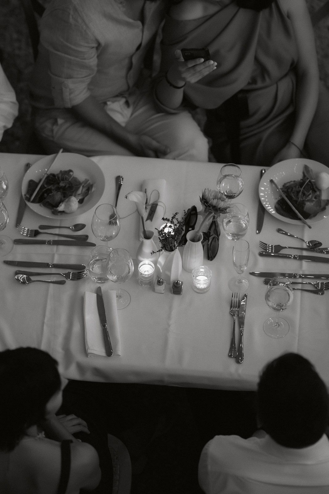 Overhead view of a formal dining table setting with white tablecloth, glassware and place settings in black and white.