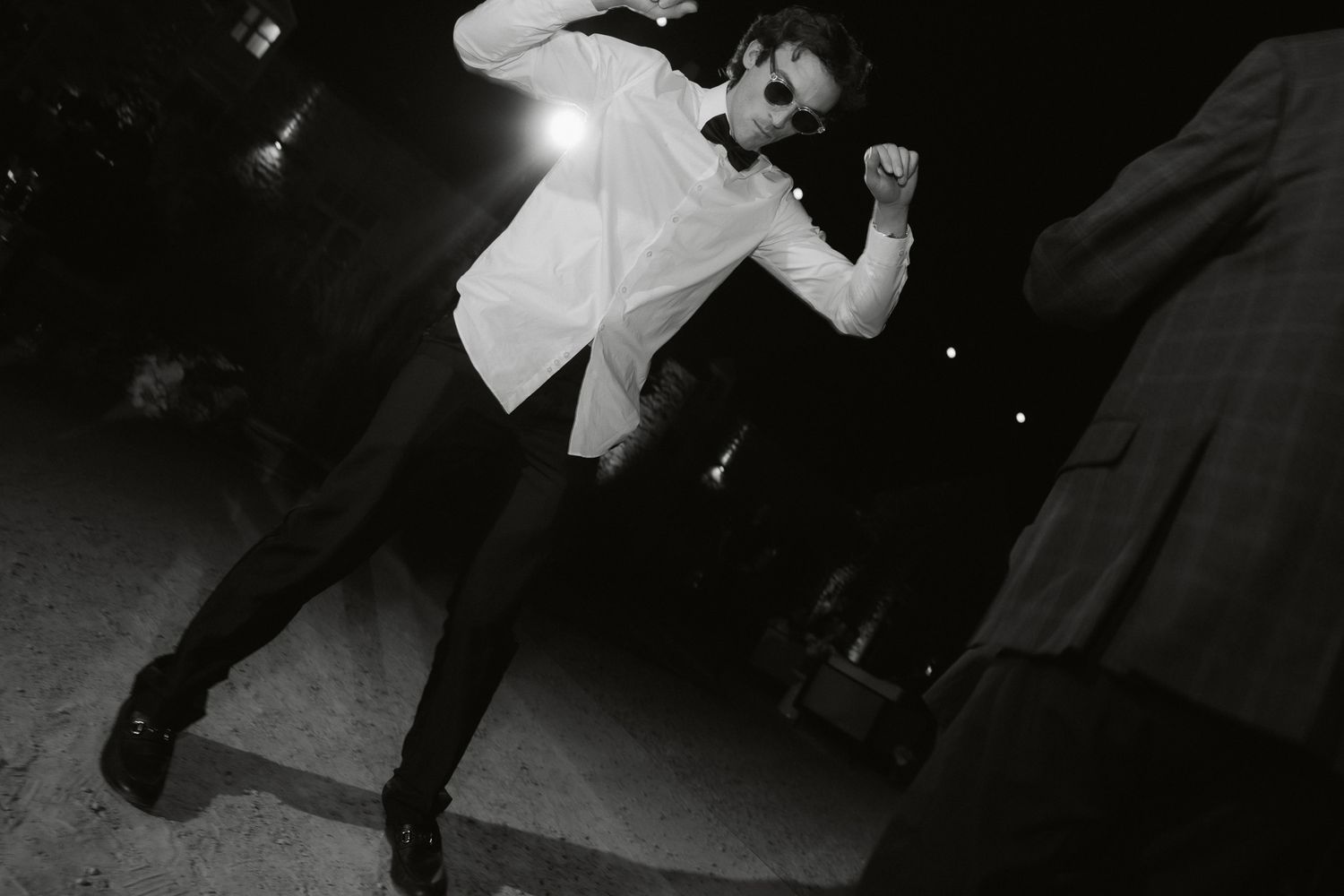 Black and white photo of a man in white shirt and bow tie dancing energetically at a formal event.