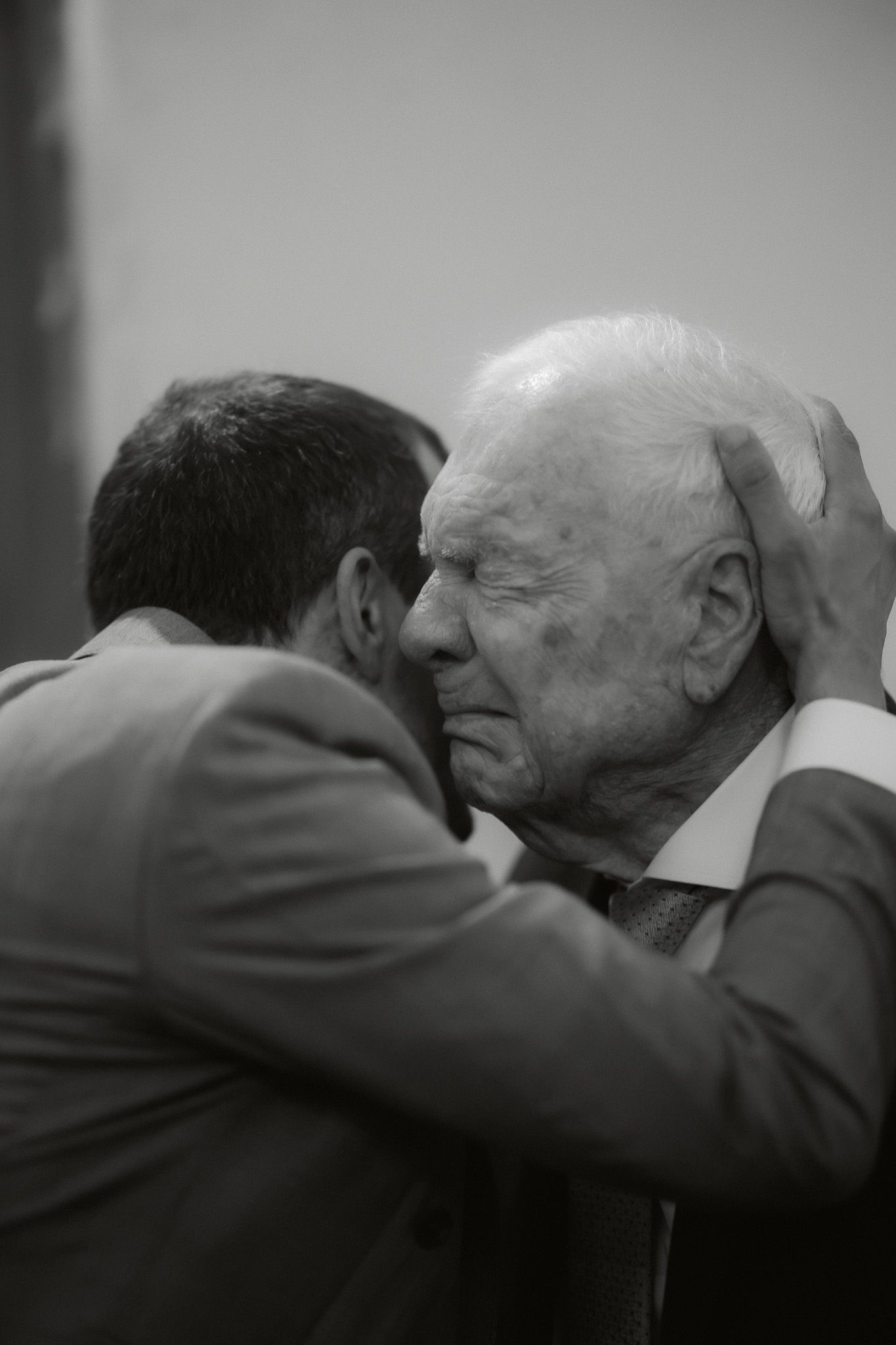 Black and white photo of two elderly and middle-aged men in suits sharing an emotional embrace.