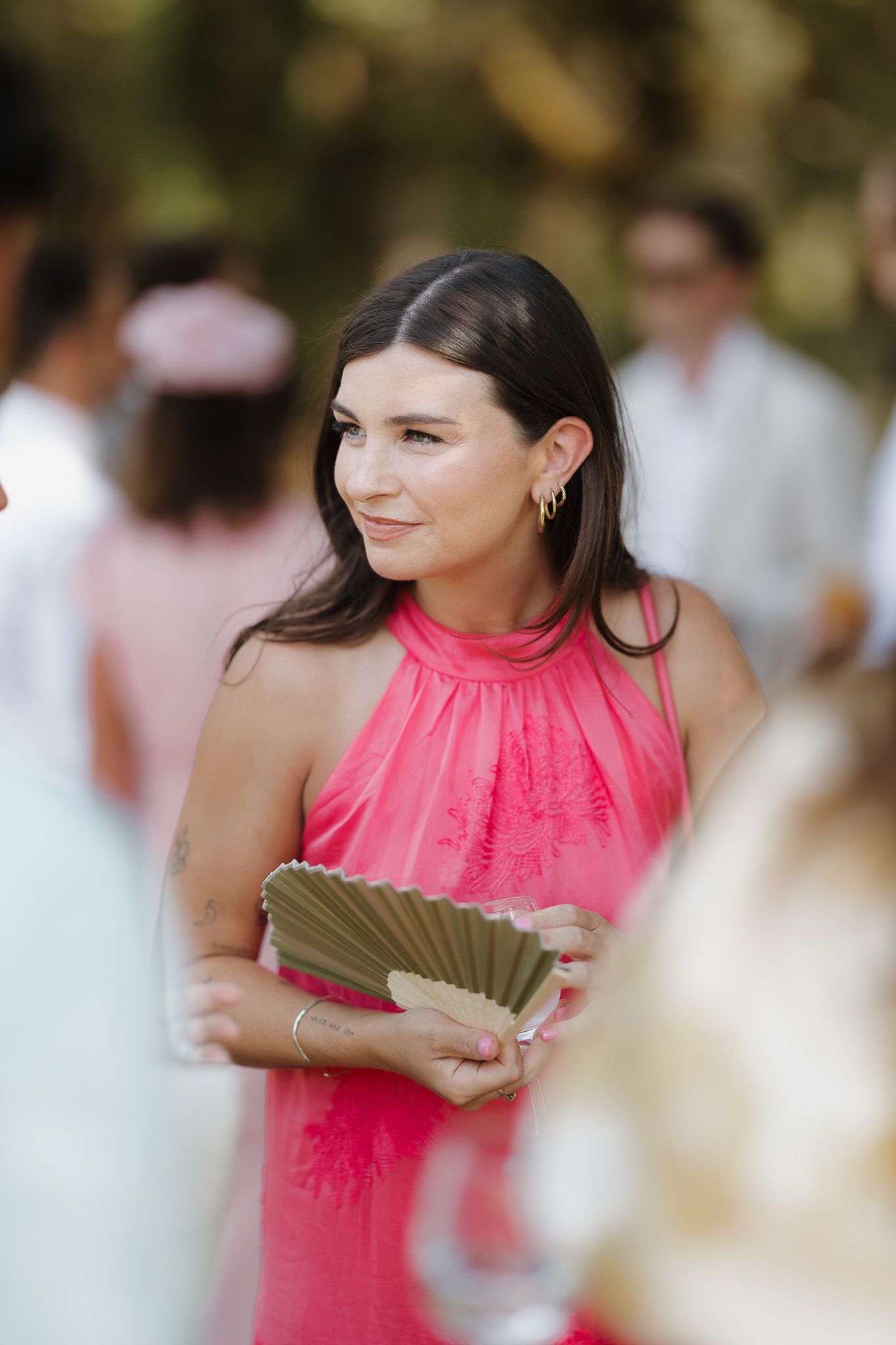Woman in pink halter dress holding a decorative fan at an outdoor event.